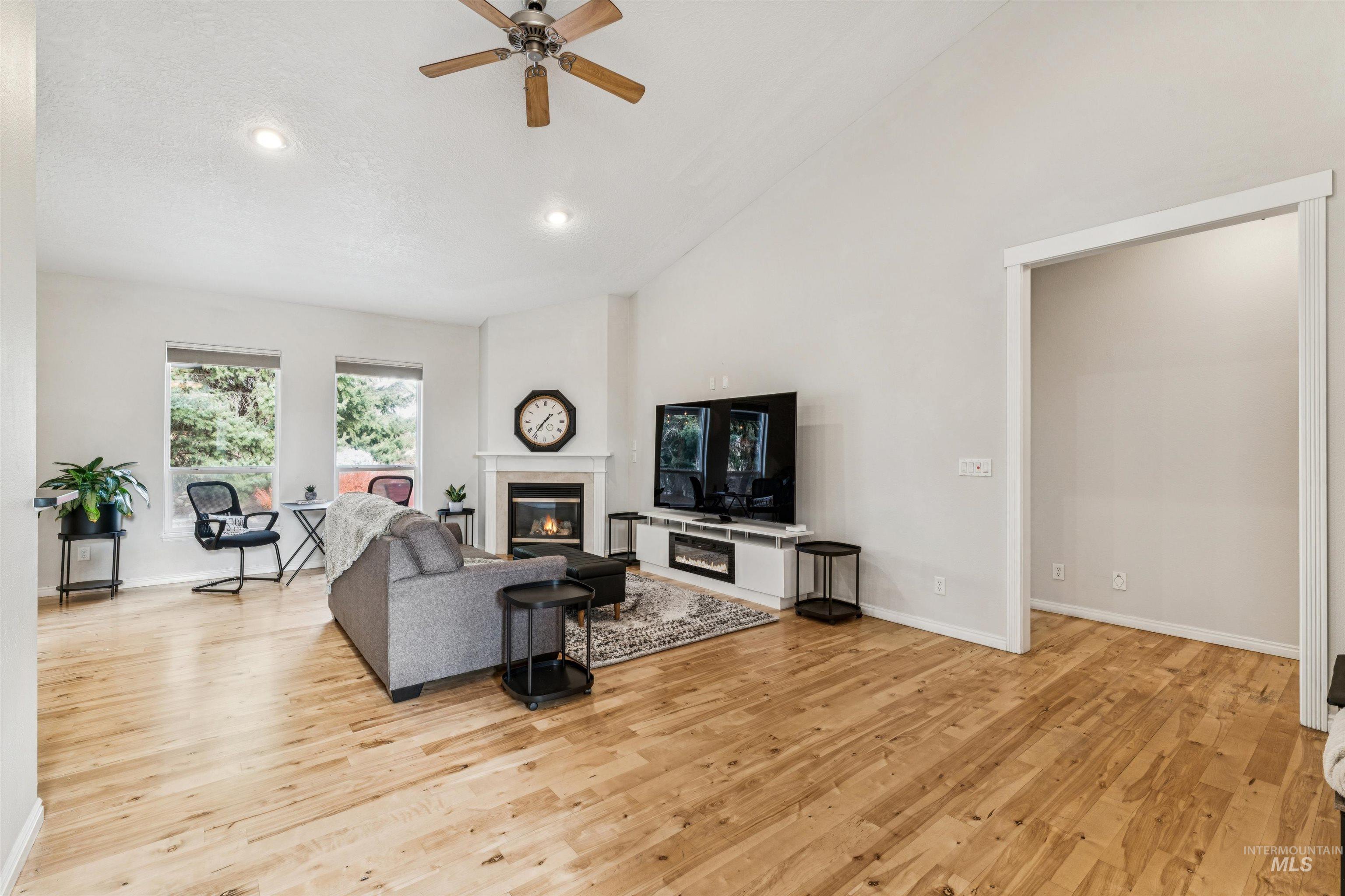 Living room with a glass covered fireplace, light wood-style floors, ceiling fan, high vaulted ceiling, and recessed lighting