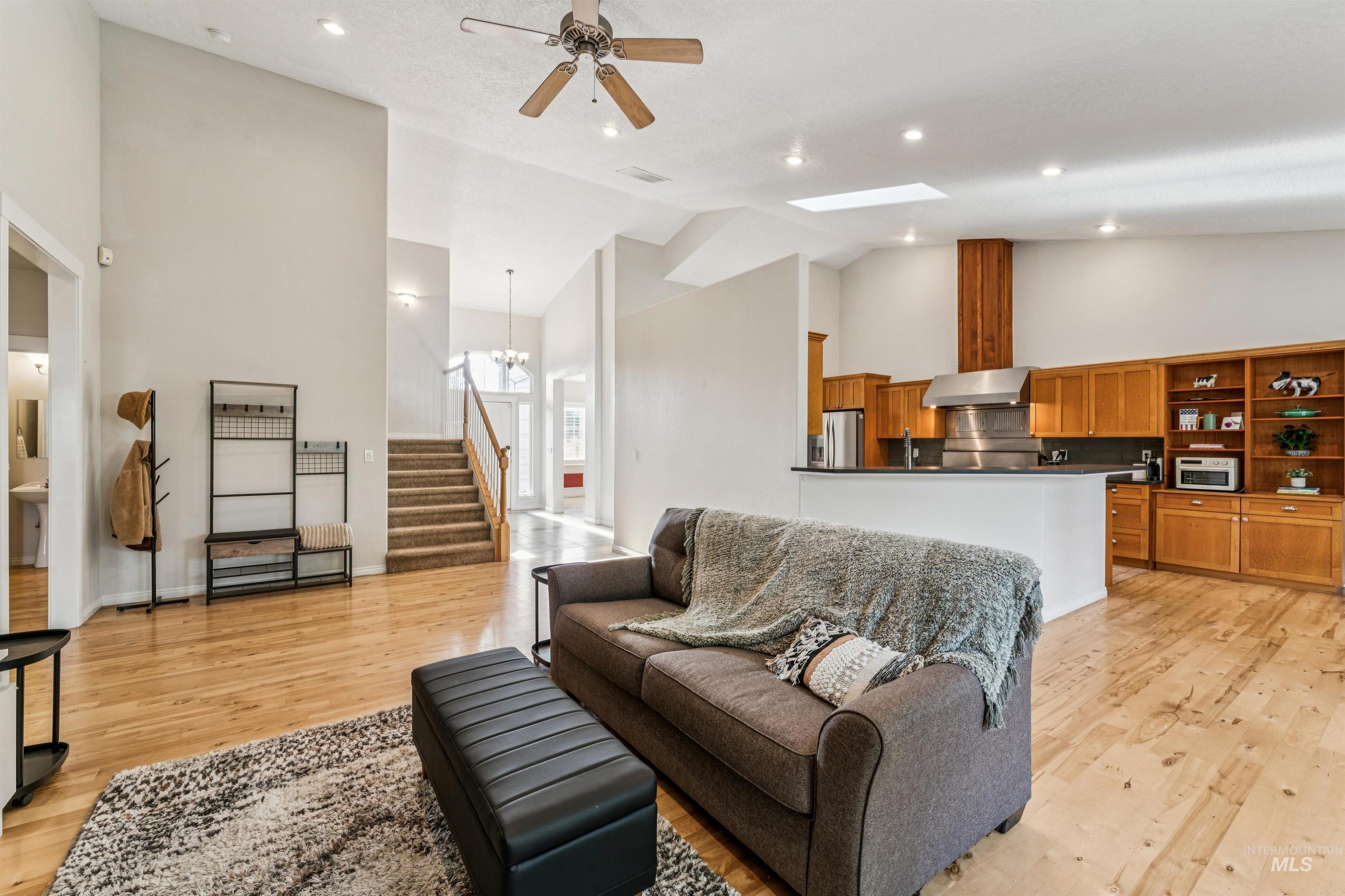 Living area with stairway, light wood-style flooring, high vaulted ceiling, ceiling fan, and a chandelier