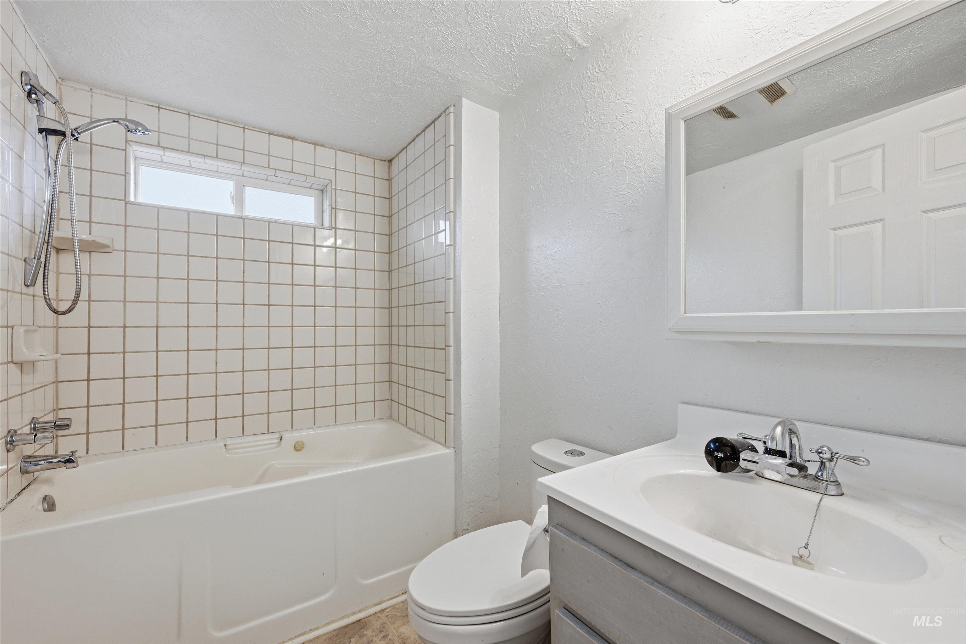 Bathroom with vanity, bathing tub / shower combination, a textured ceiling, and a textured wall