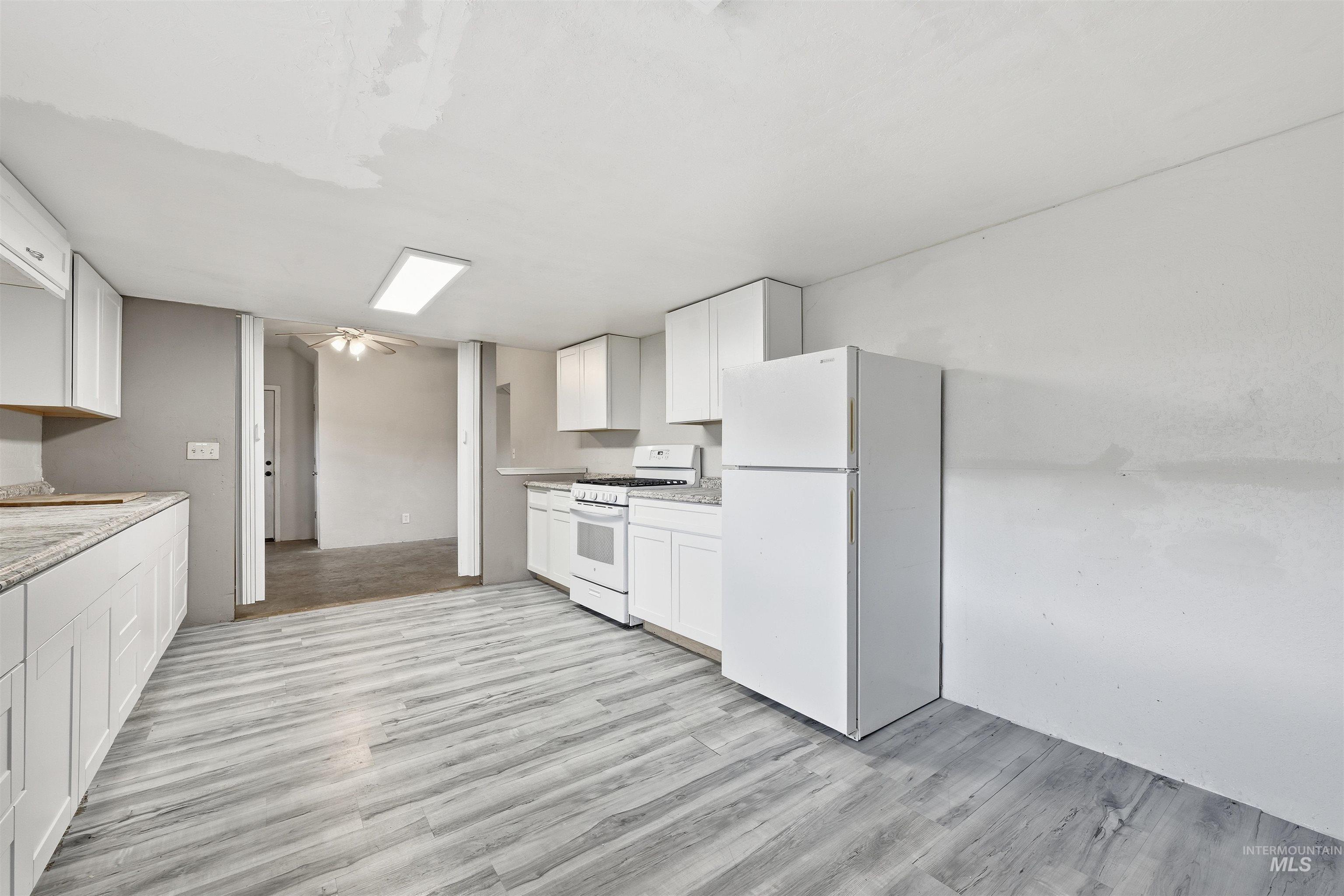 Kitchen featuring white appliances, white cabinets, and light wood-style floors