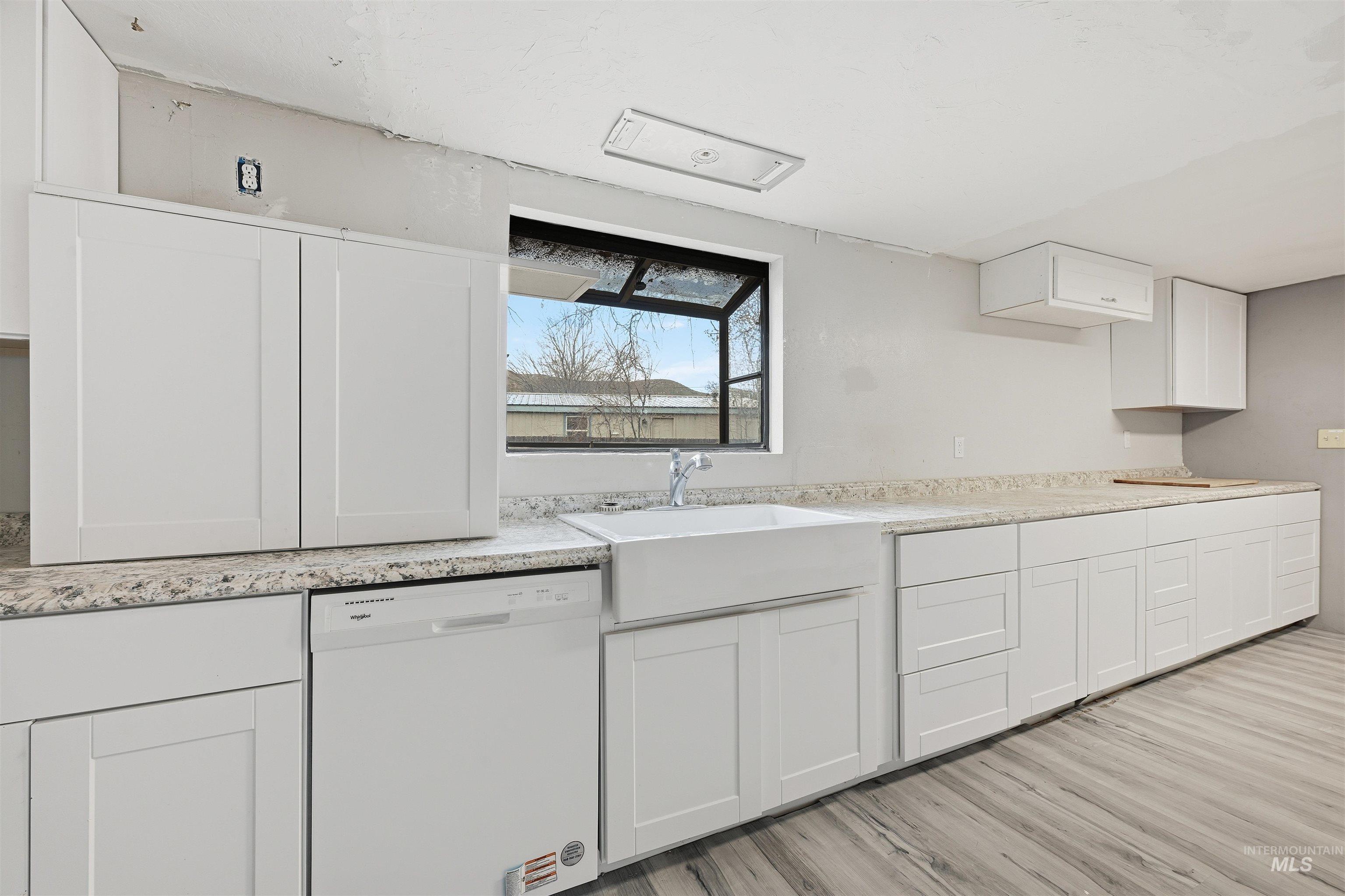 Kitchen with white cabinetry, dishwasher, light wood-style flooring, and light stone counters