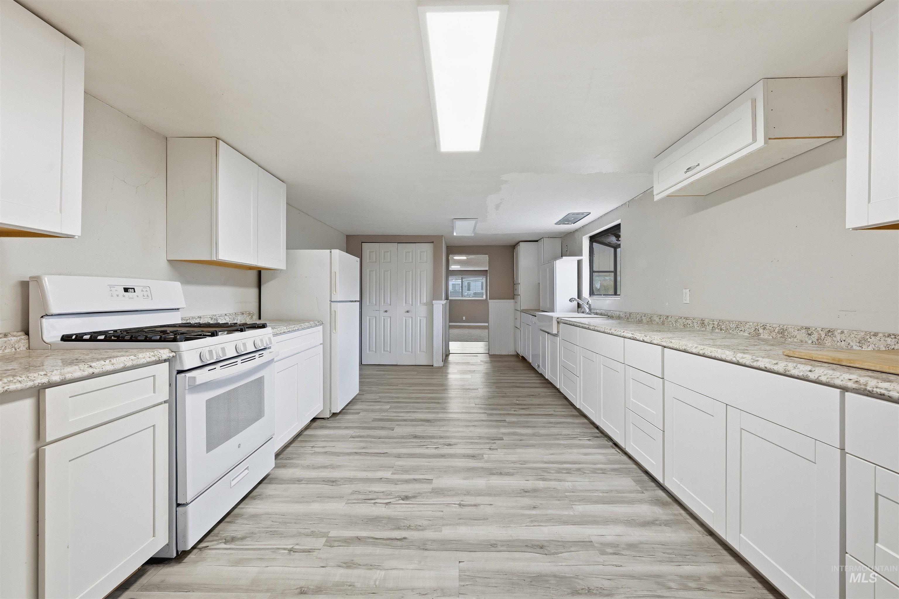 Kitchen featuring white appliances, white cabinets, light wood-style floors, and light stone counters