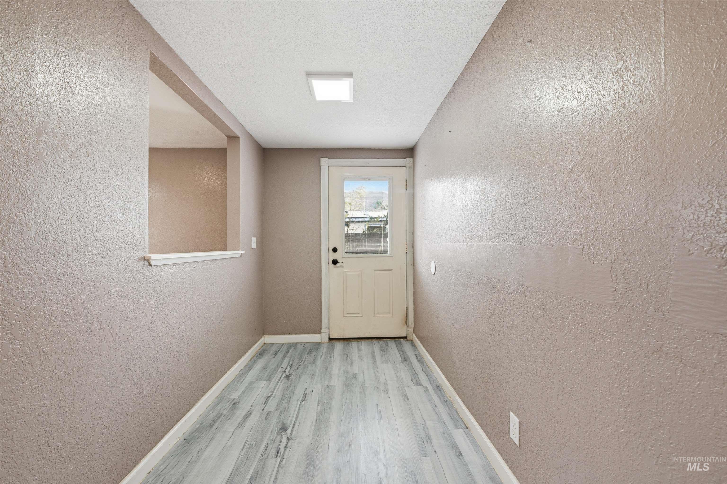 Doorway featuring a textured wall, wood finished floors, and a textured ceiling