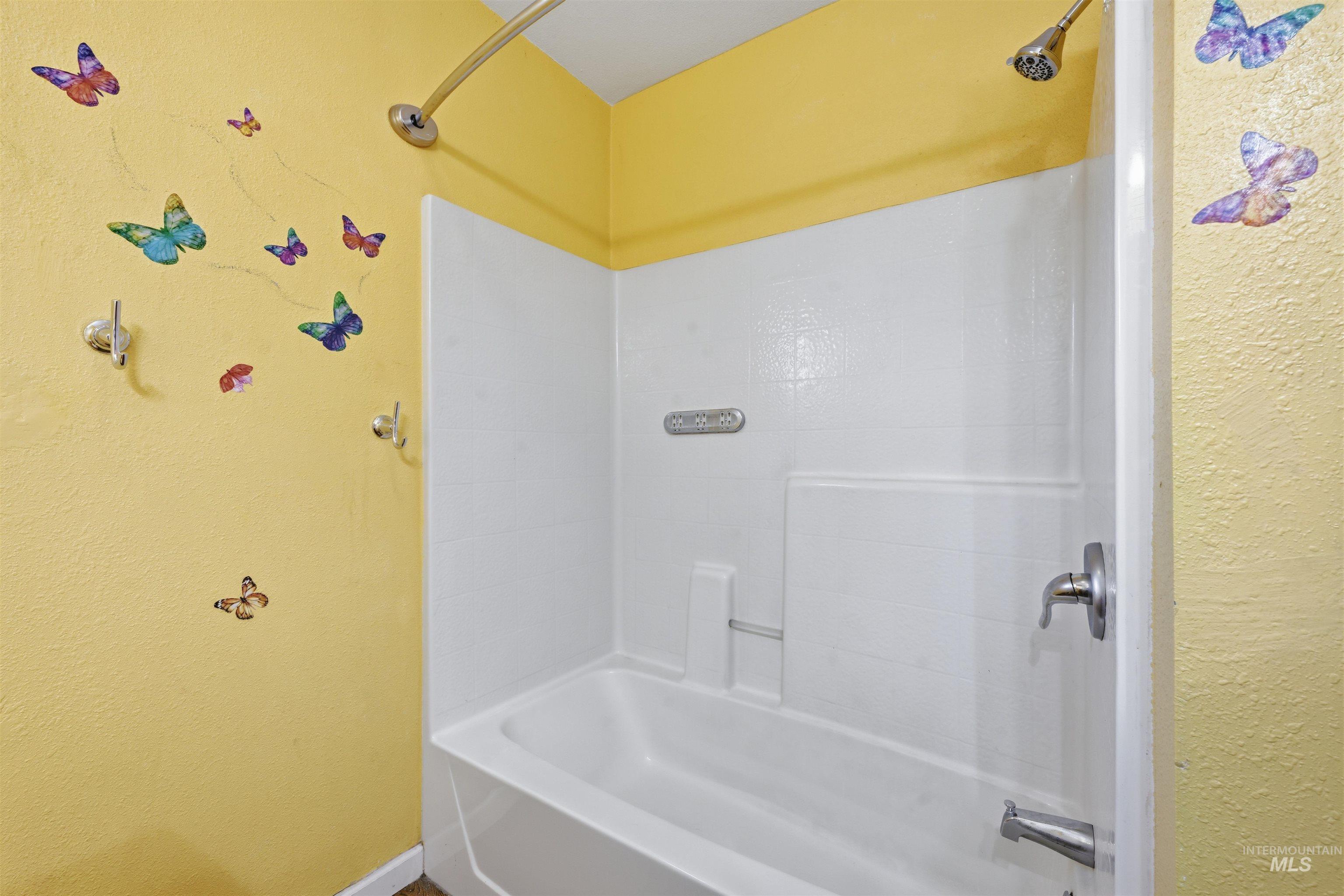 Bathroom with a textured wall and shower / bathtub combination