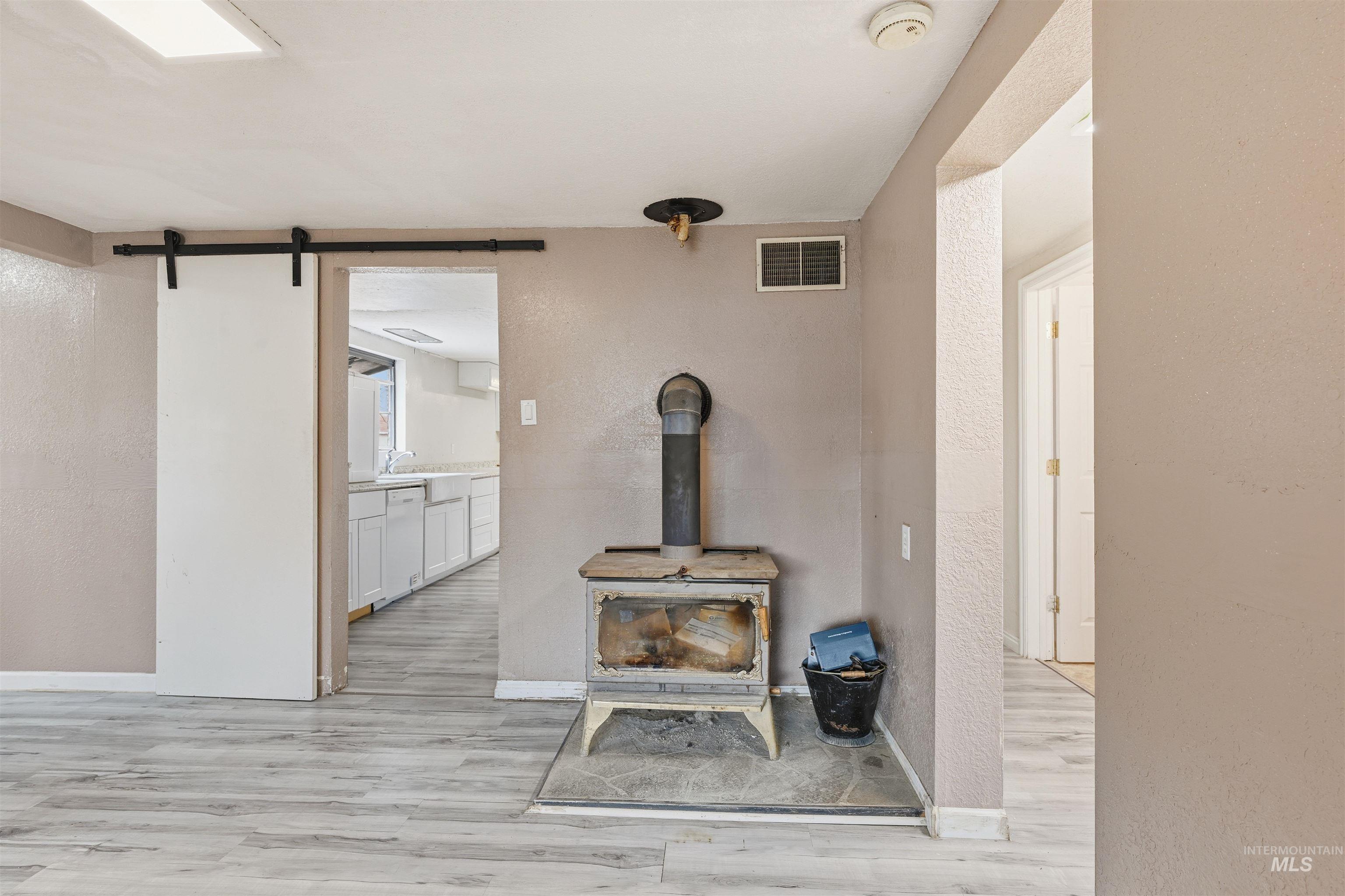 Detailed view of a textured wall, a wood stove, wood finished floors, a barn door, and white dishwasher