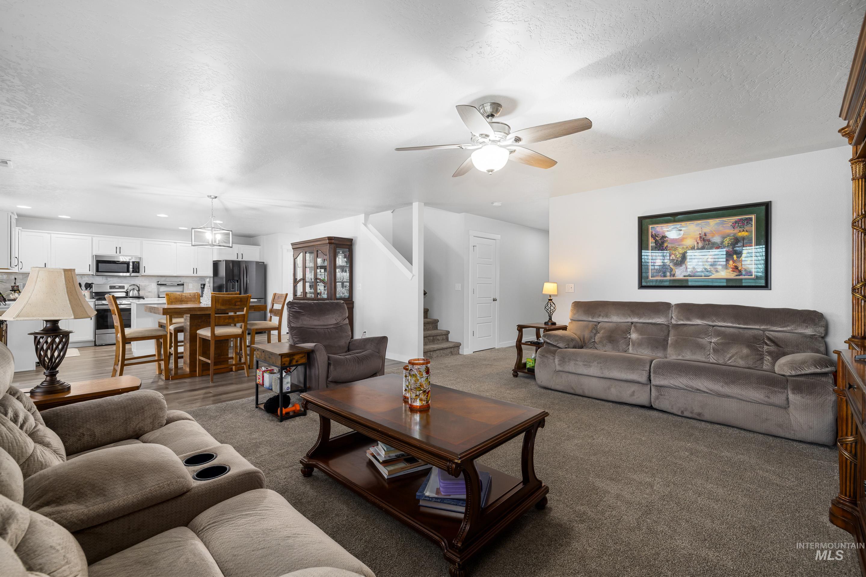 Carpeted living area featuring a ceiling fan, stairs, a textured ceiling, and recessed lighting