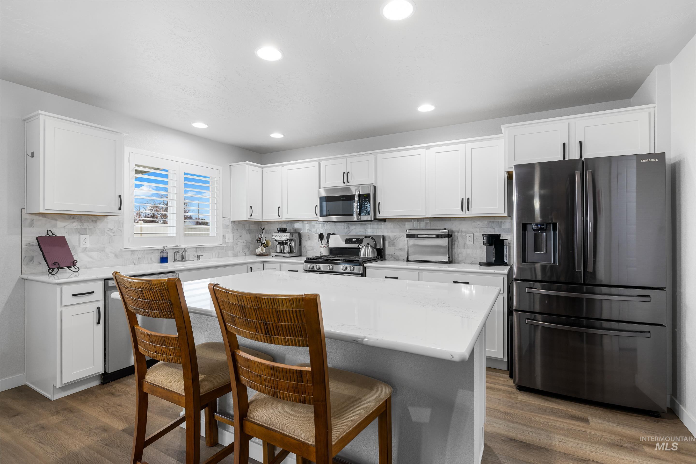 Kitchen with stainless steel appliances, white cabinets, a kitchen bar, dark wood-type flooring, and light stone counters