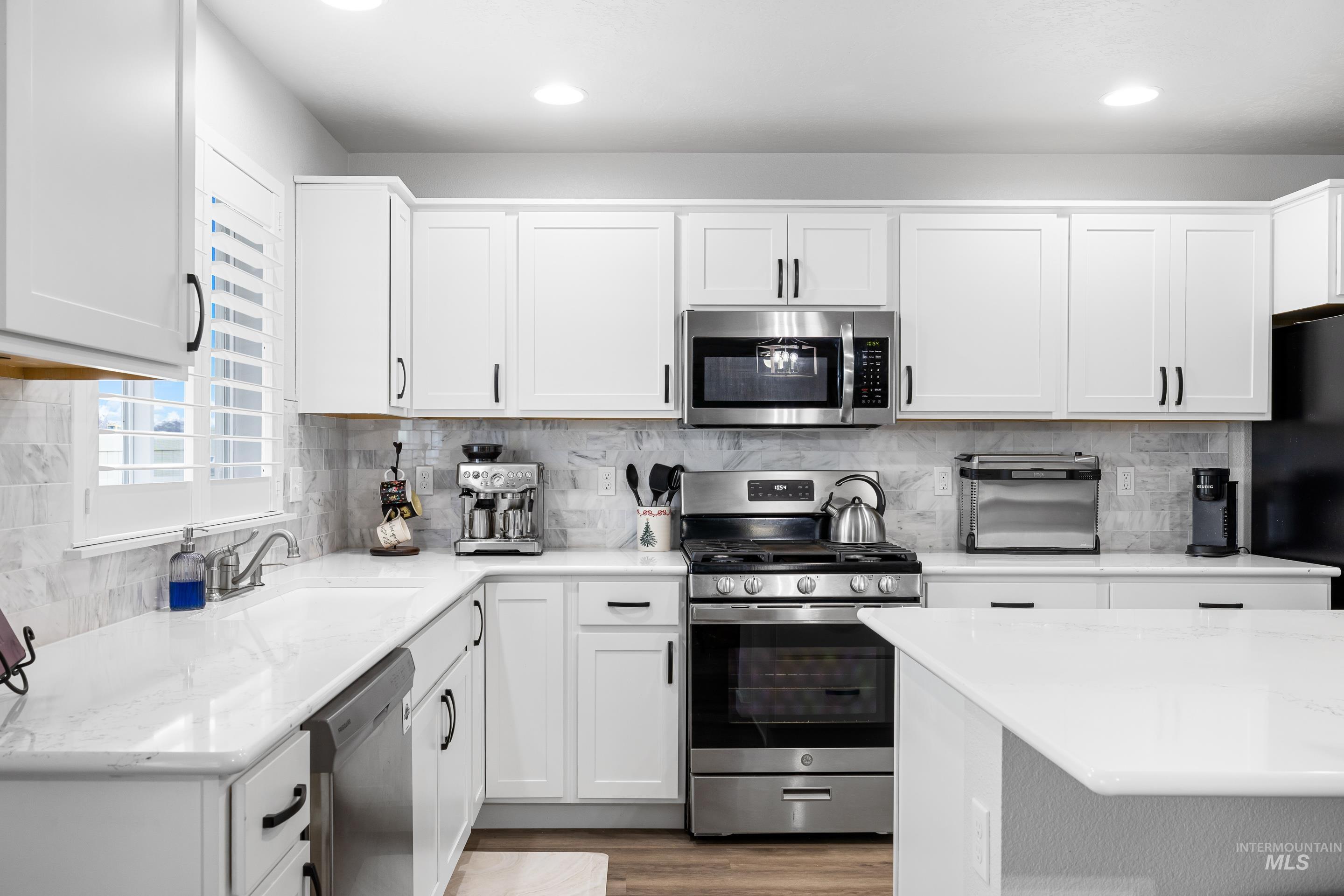 Kitchen featuring stainless steel appliances, white cabinets, light stone countertops, decorative backsplash, and recessed lighting