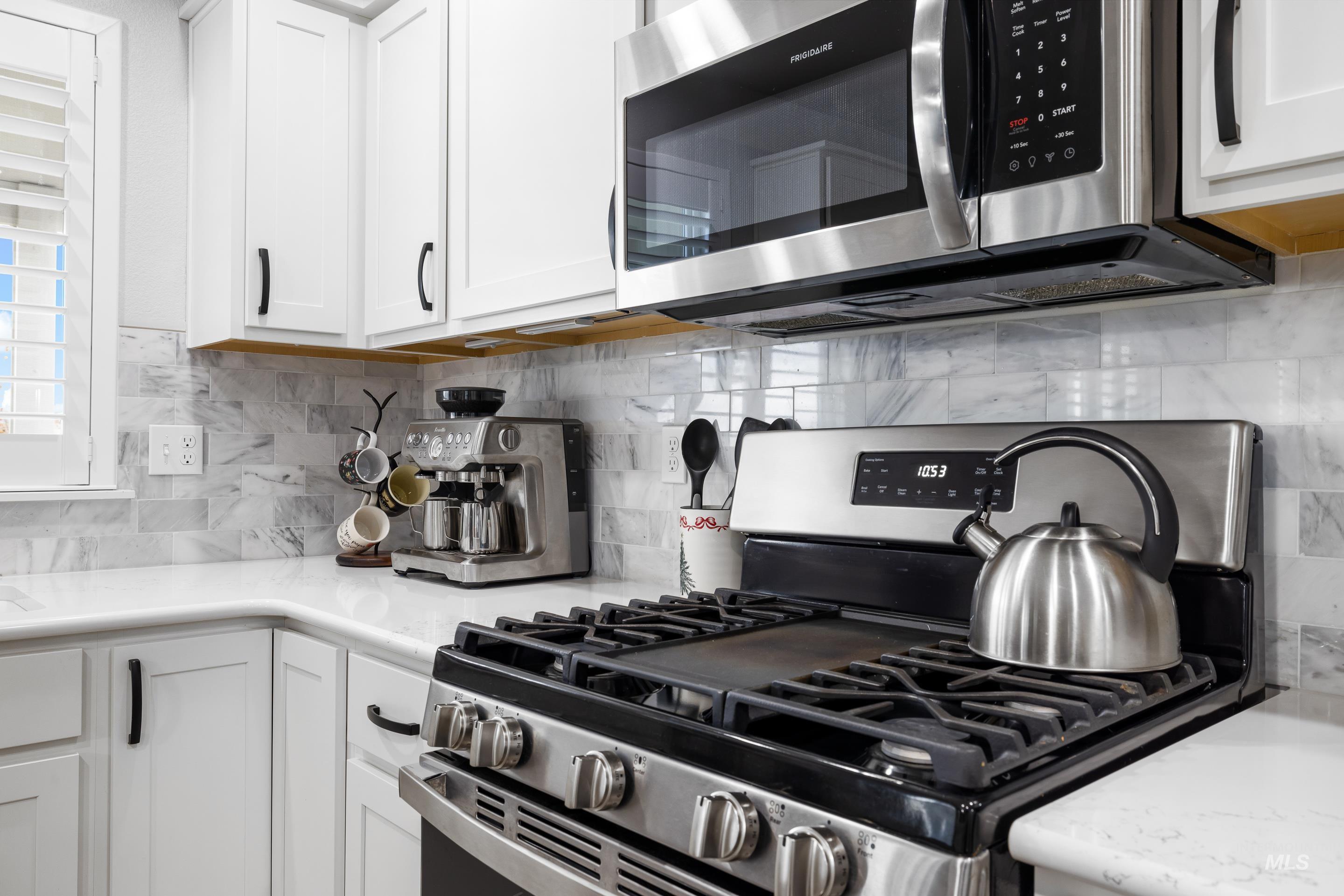 Kitchen with appliances with stainless steel finishes, tasteful backsplash, white cabinetry, and light stone counters
