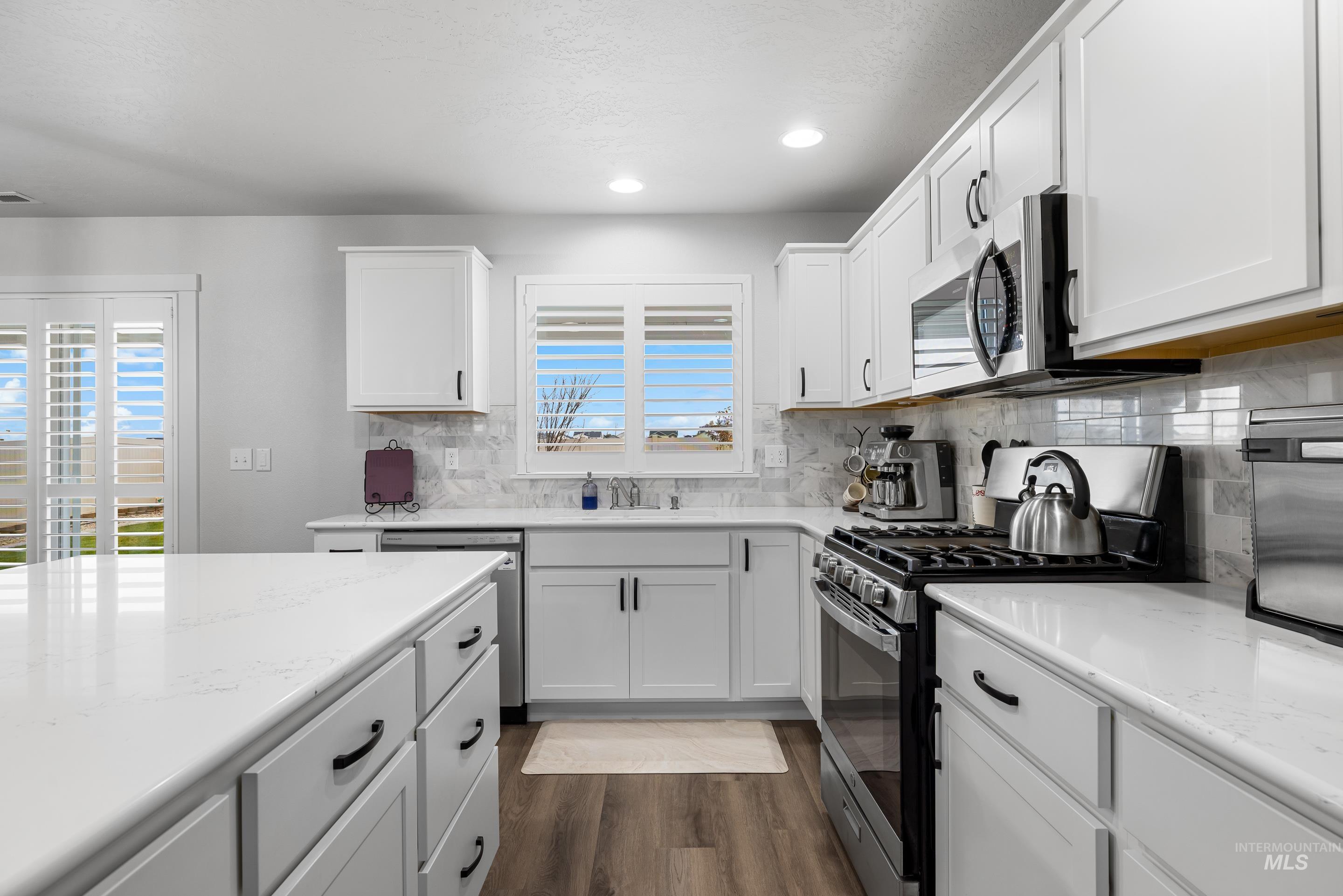 Kitchen with stainless steel appliances, white cabinetry, recessed lighting, dark wood-style flooring, and light stone countertops