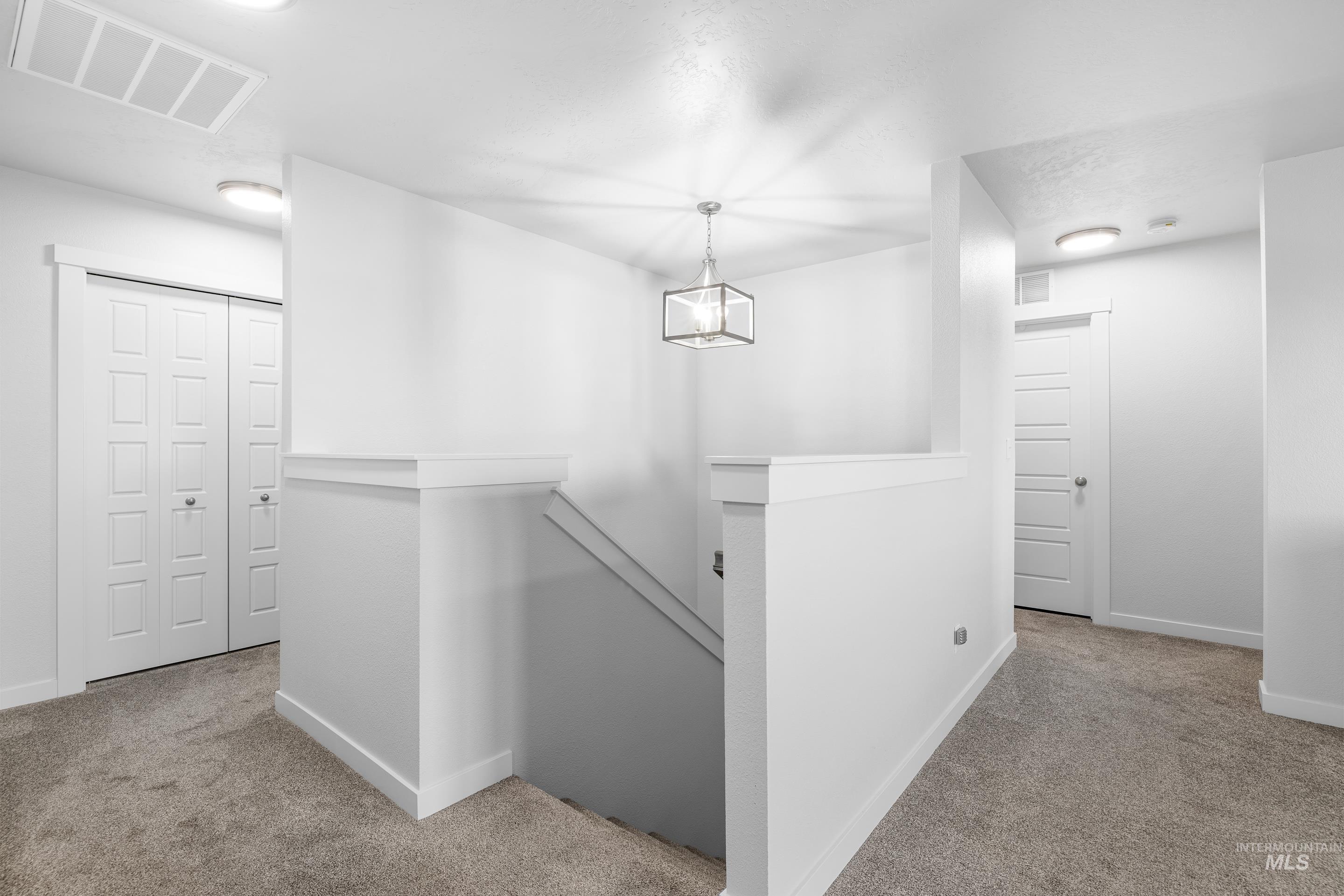 Corridor with an upstairs landing, light carpet, and a chandelier