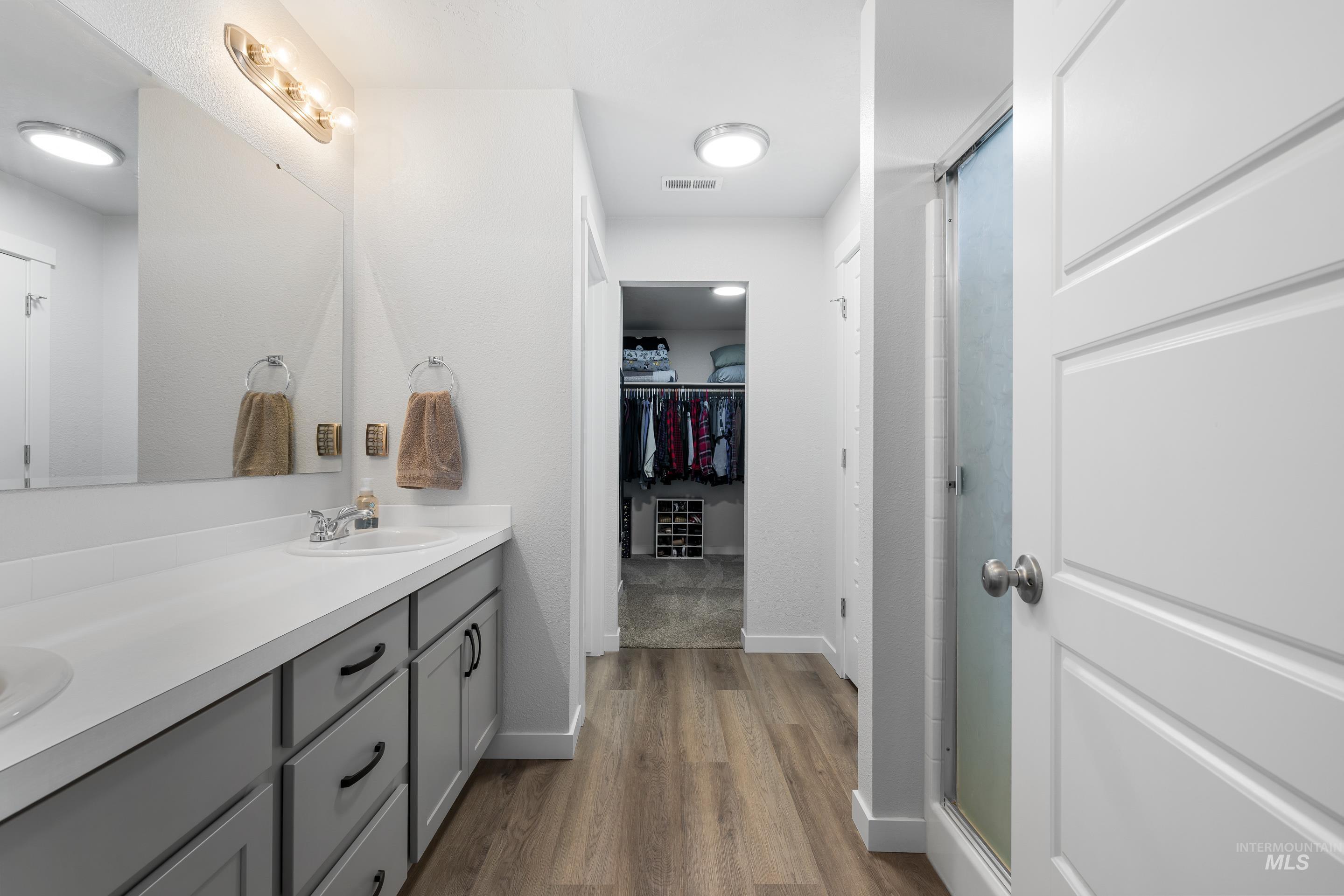 Bathroom featuring double vanity, a stall shower, dark wood-style flooring, and a walk in closet