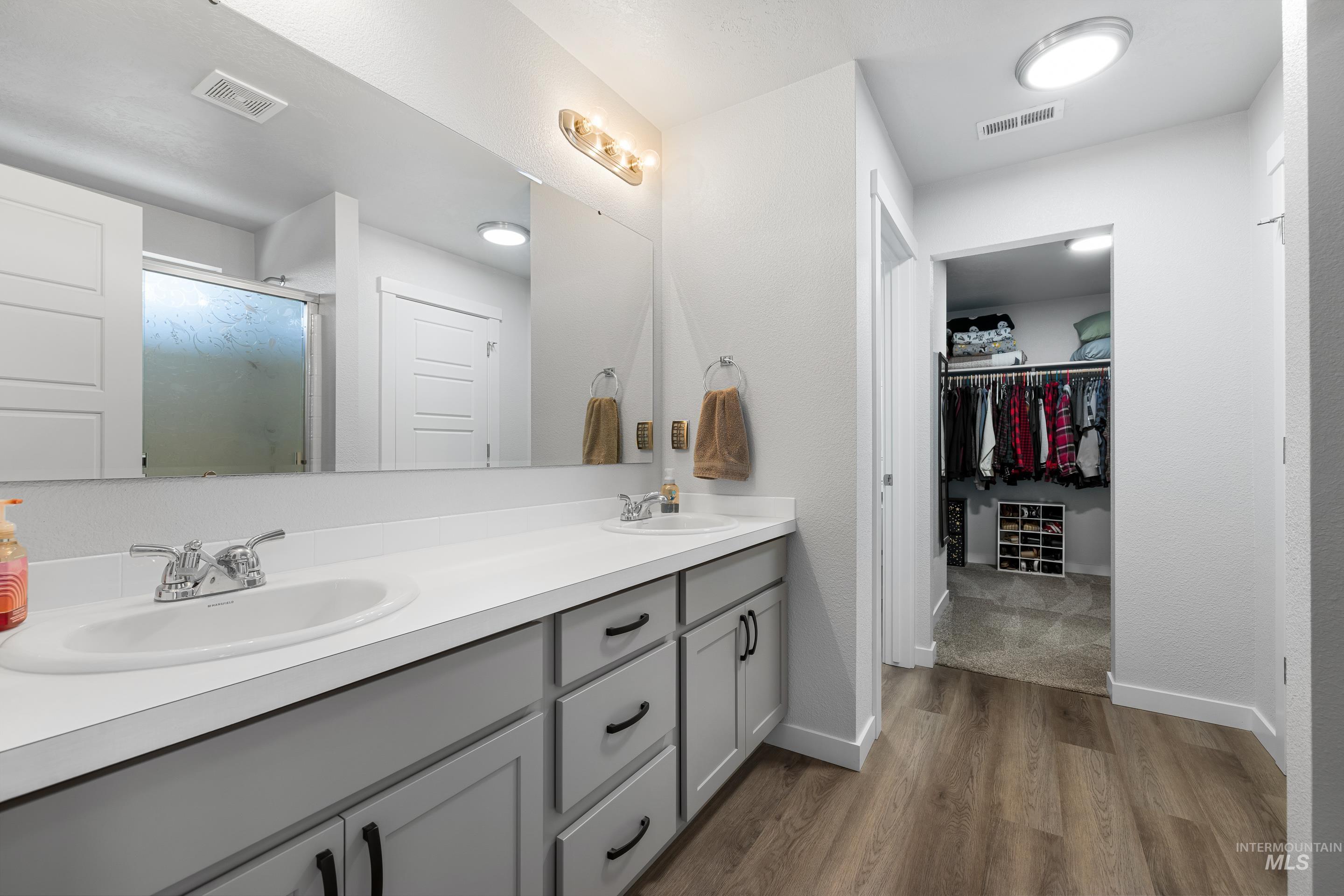 Bathroom with double vanity, a shower stall, a walk in closet, and dark wood finished floors