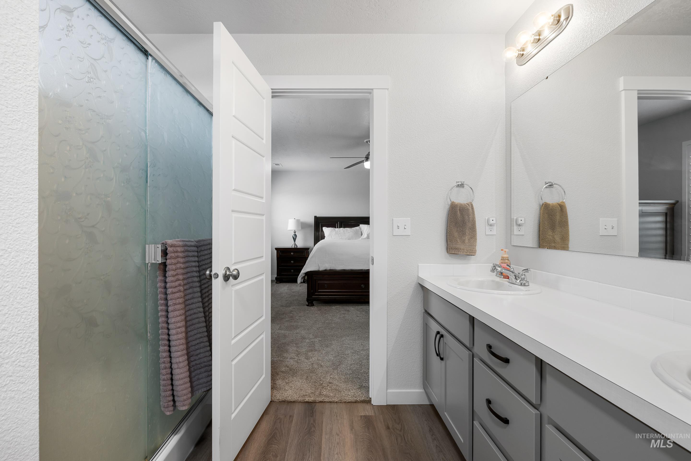 Ensuite bathroom featuring double vanity, a stall shower, dark wood-type flooring, and ceiling fan