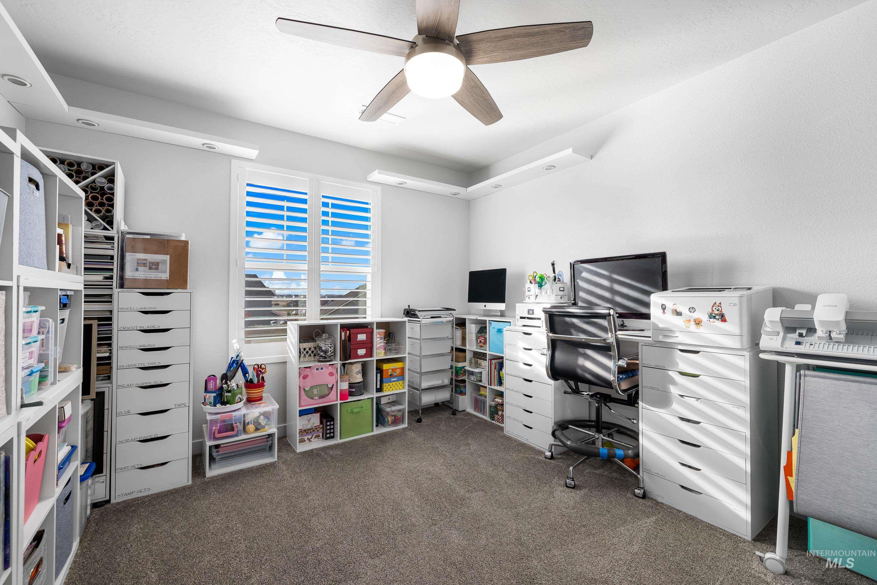 Home office with a ceiling fan and dark colored carpet