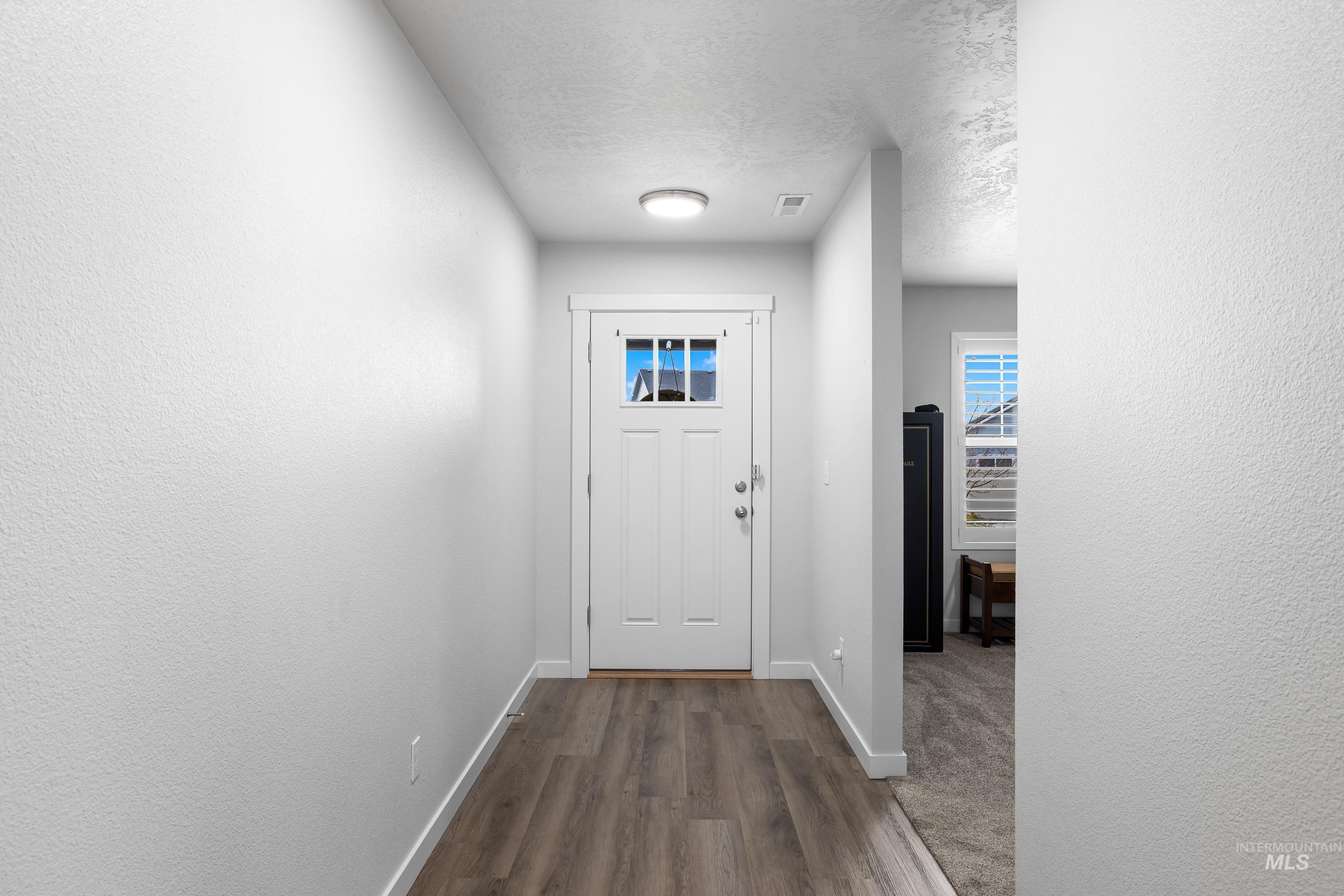 Doorway featuring a textured ceiling, wood finished floors, and a textured wall
