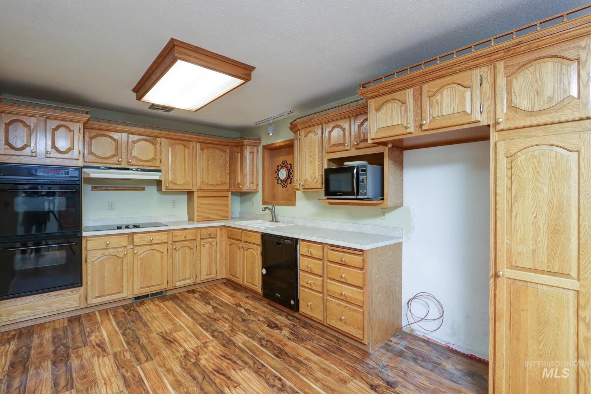 Kitchen featuring black appliances, light countertops, dark wood-type flooring, under cabinet range hood, and light brown cabinetry