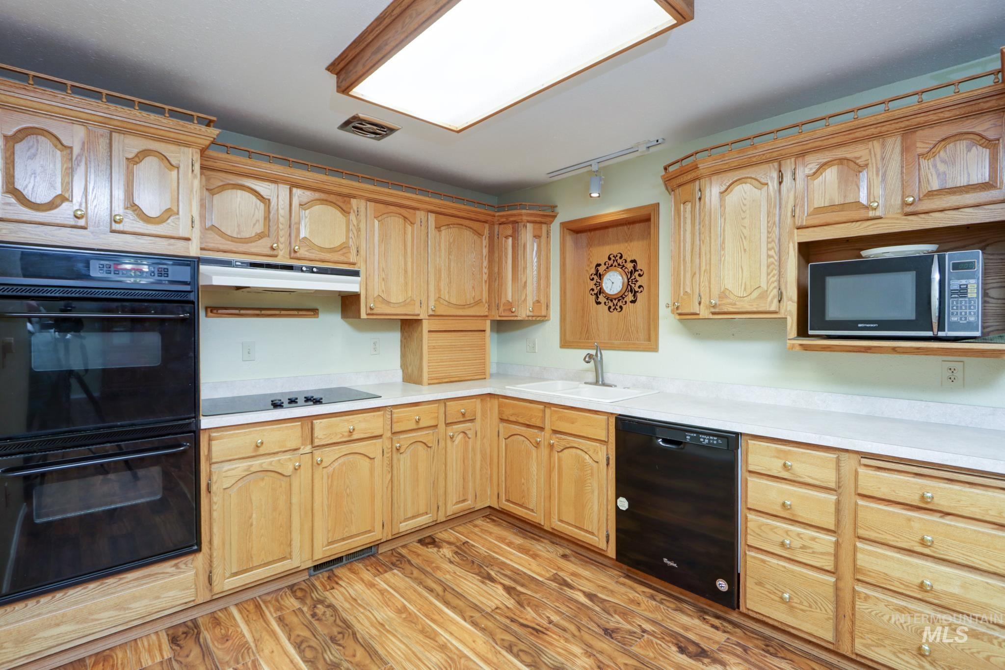 Kitchen featuring black appliances, light countertops, light wood-type flooring, under cabinet range hood, and rail lighting