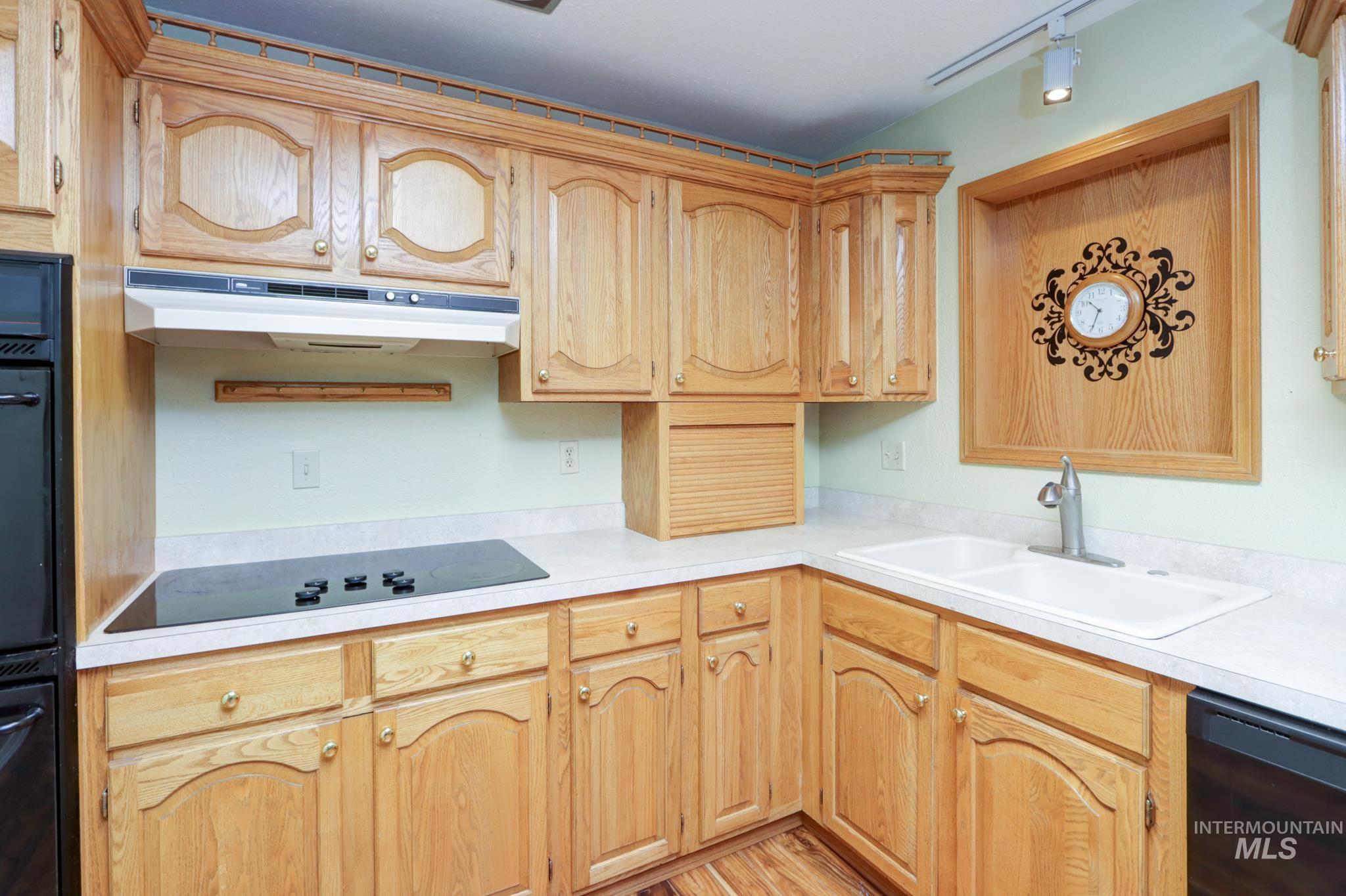Kitchen featuring light countertops, black appliances, under cabinet range hood, light brown cabinets, and light wood finished floors