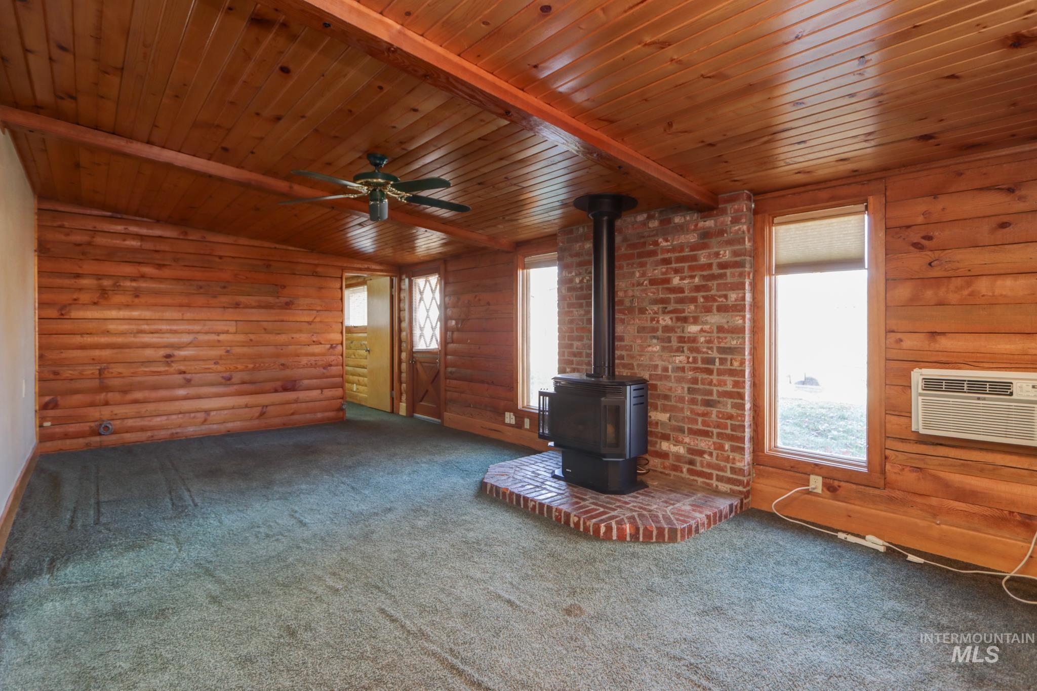 Unfurnished living room featuring a wood stove, wood ceiling, healthy amount of natural light, carpet flooring, and rustic walls