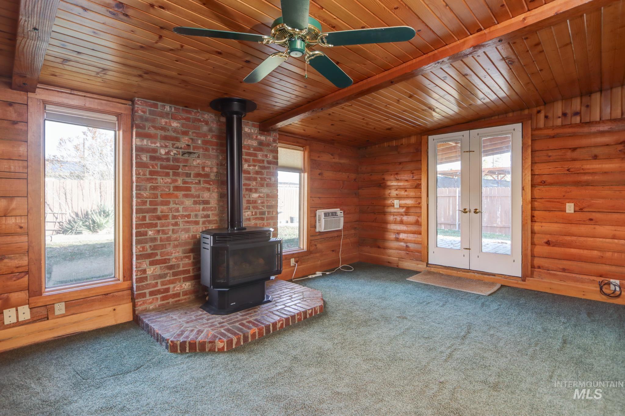 Unfurnished living room with a wood stove, carpet, a wooden ceiling with exposed beams, wooden walls, and an AC wall unit