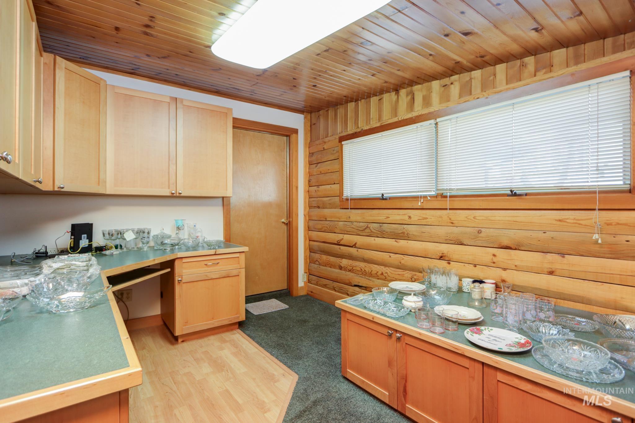 Kitchen with built in desk, rustic walls, light brown cabinets, wooden ceiling, and light wood finished floors