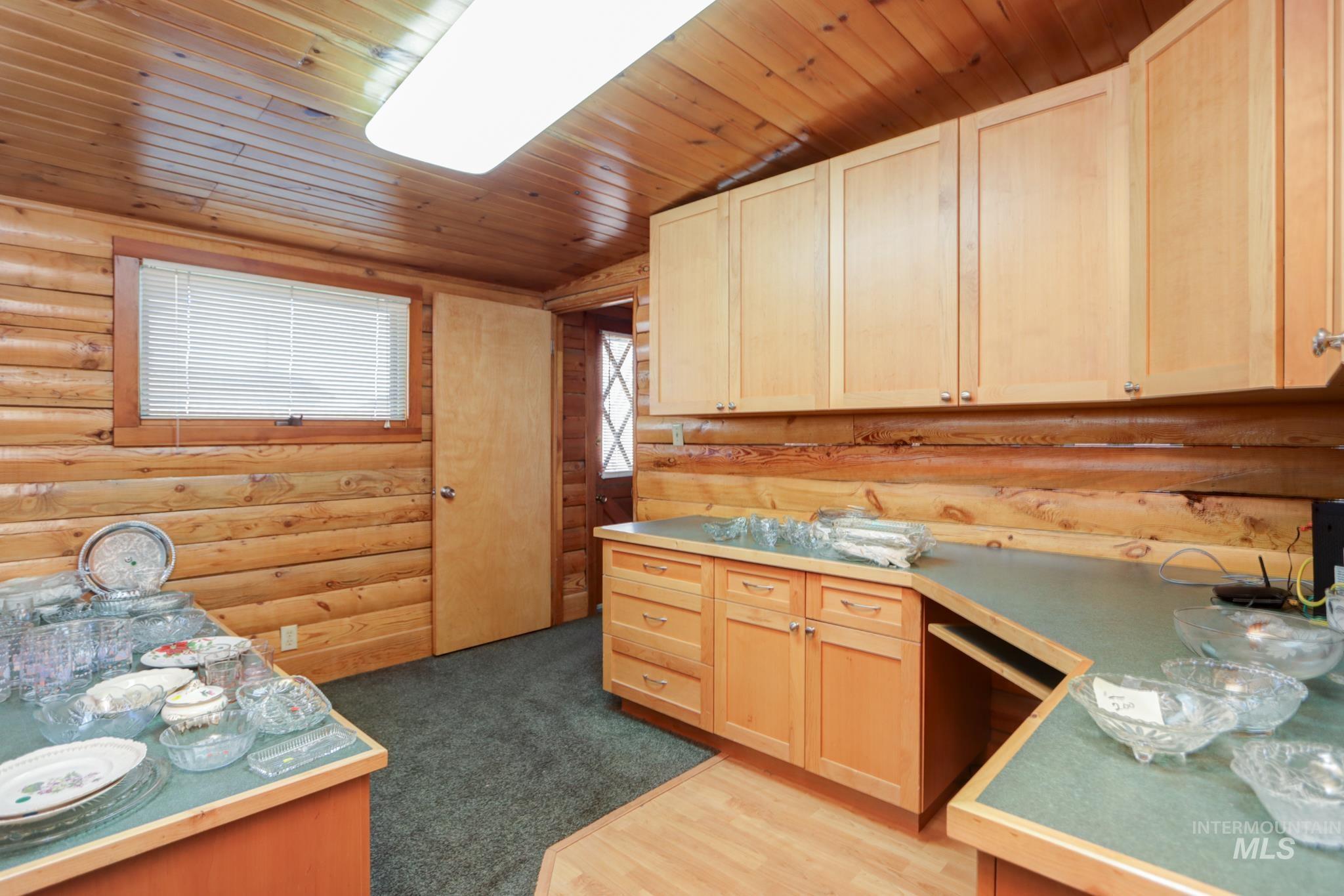 Kitchen with light brown cabinets, log walls, wood ceiling, dark carpet, and light countertops