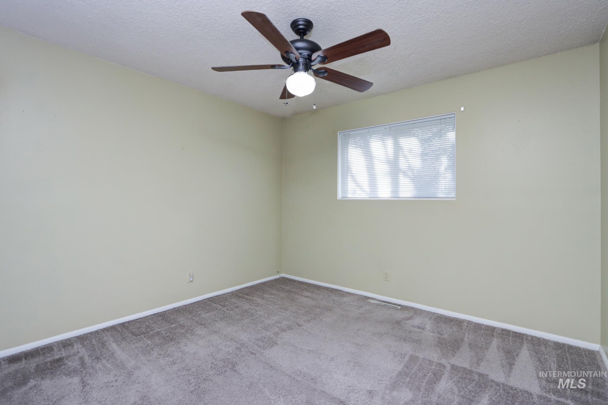 Carpeted empty room featuring a textured ceiling and ceiling fan