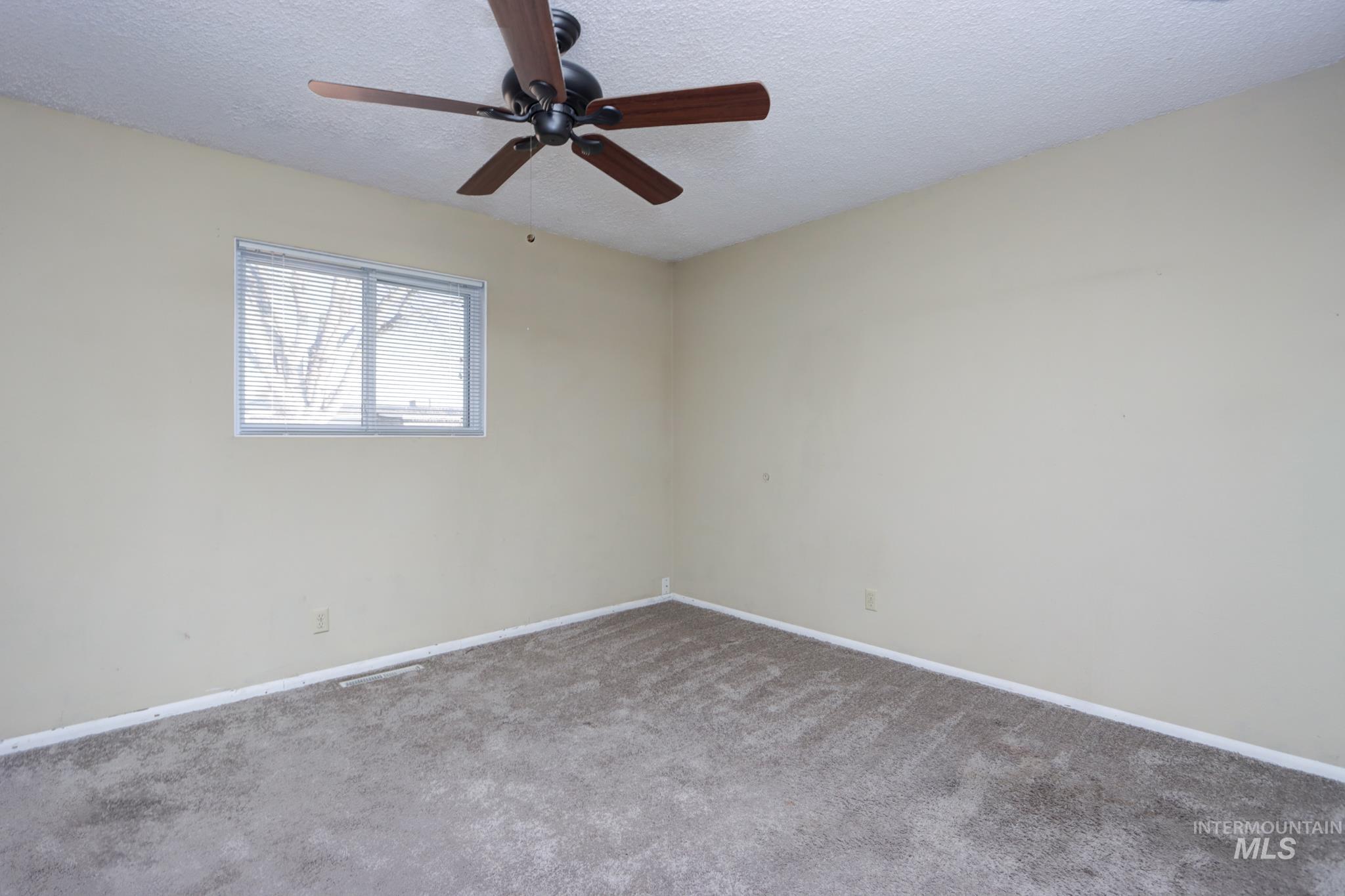 Empty room featuring a textured ceiling, ceiling fan, and carpet flooring