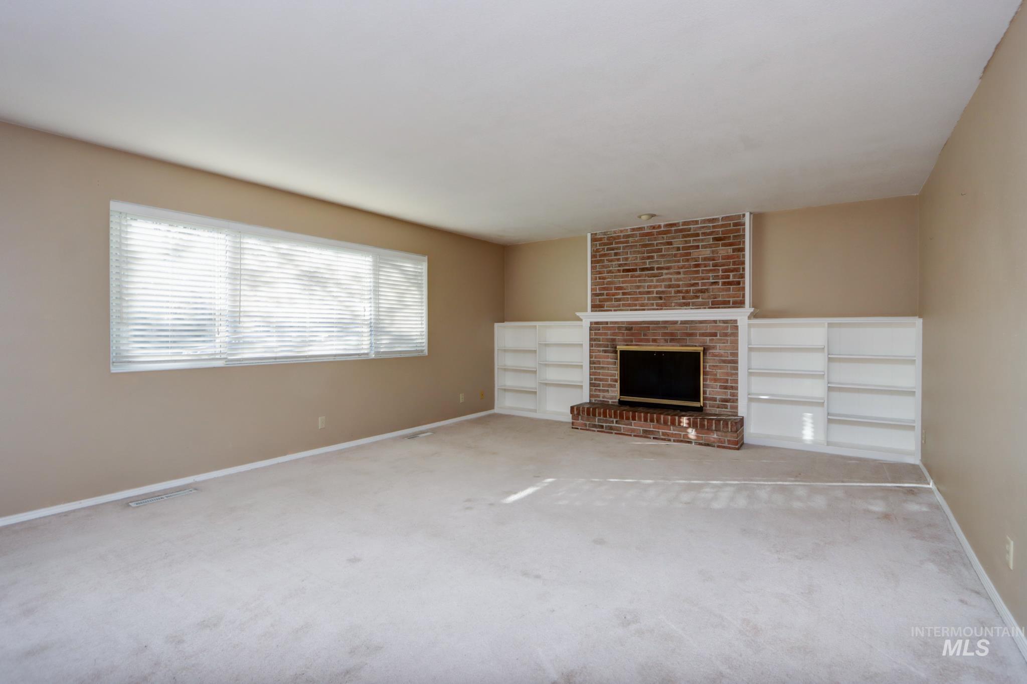 Unfurnished living room with a brick fireplace and carpet floors