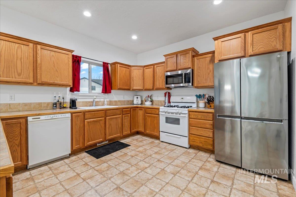 Kitchen with stainless steel appliances, light countertops, brown cabinetry, and recessed lighting