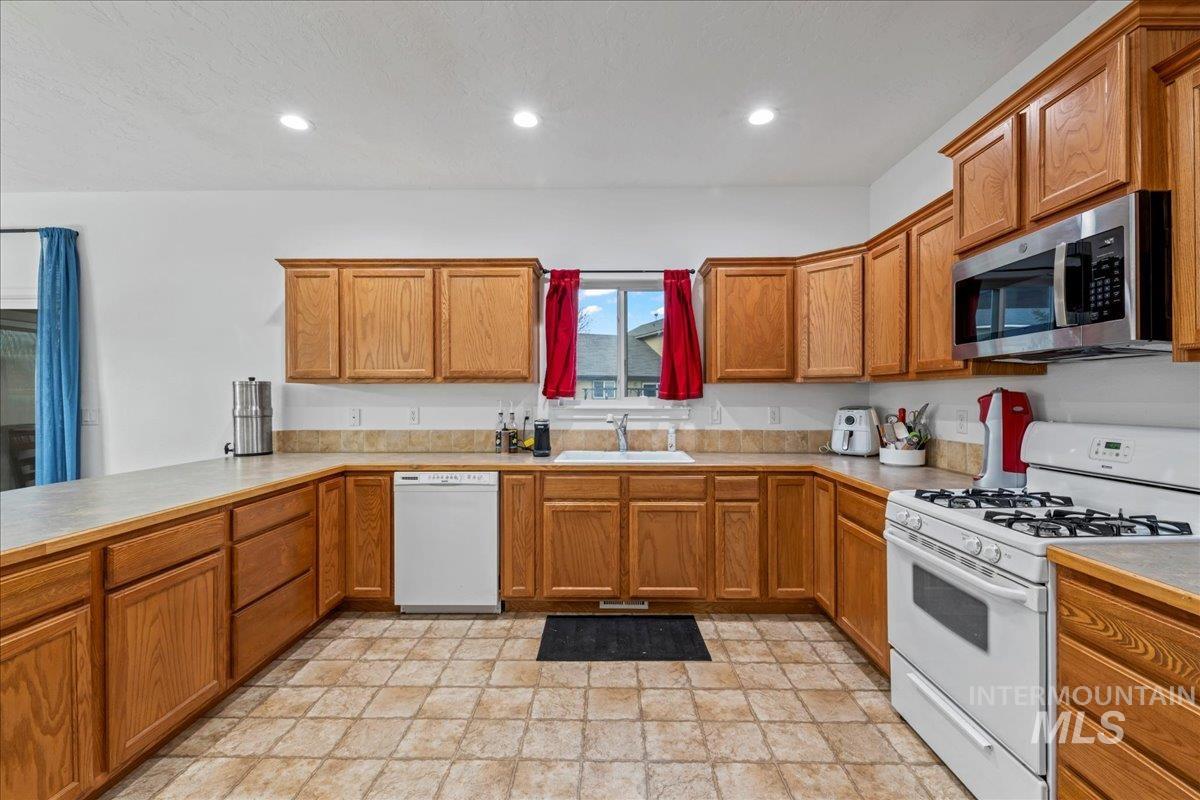 Kitchen with white appliances, brown cabinets, light countertops, recessed lighting, and stone finish floors