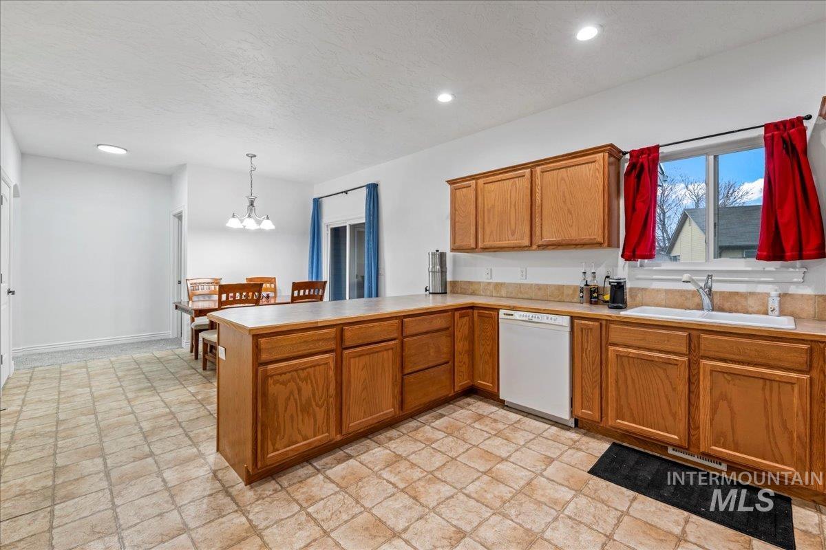 Kitchen with brown cabinets, a peninsula, white dishwasher, hanging light fixtures, and light countertops