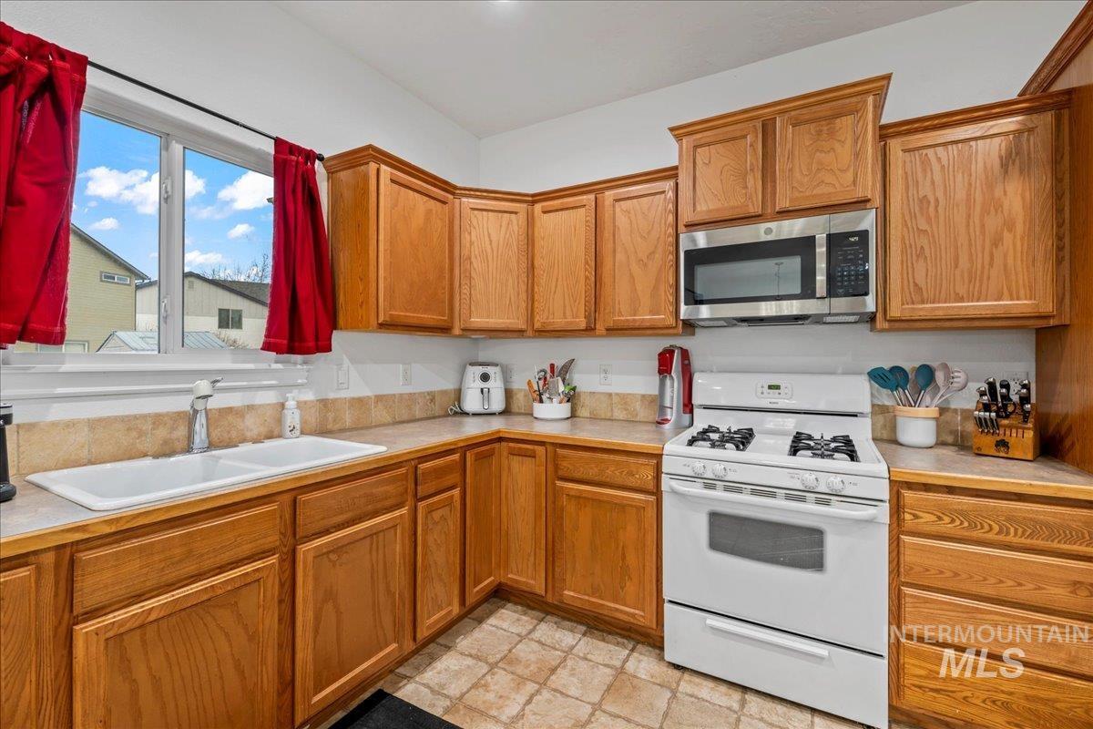 Kitchen featuring white range with gas stovetop, stainless steel microwave, and brown cabinetry