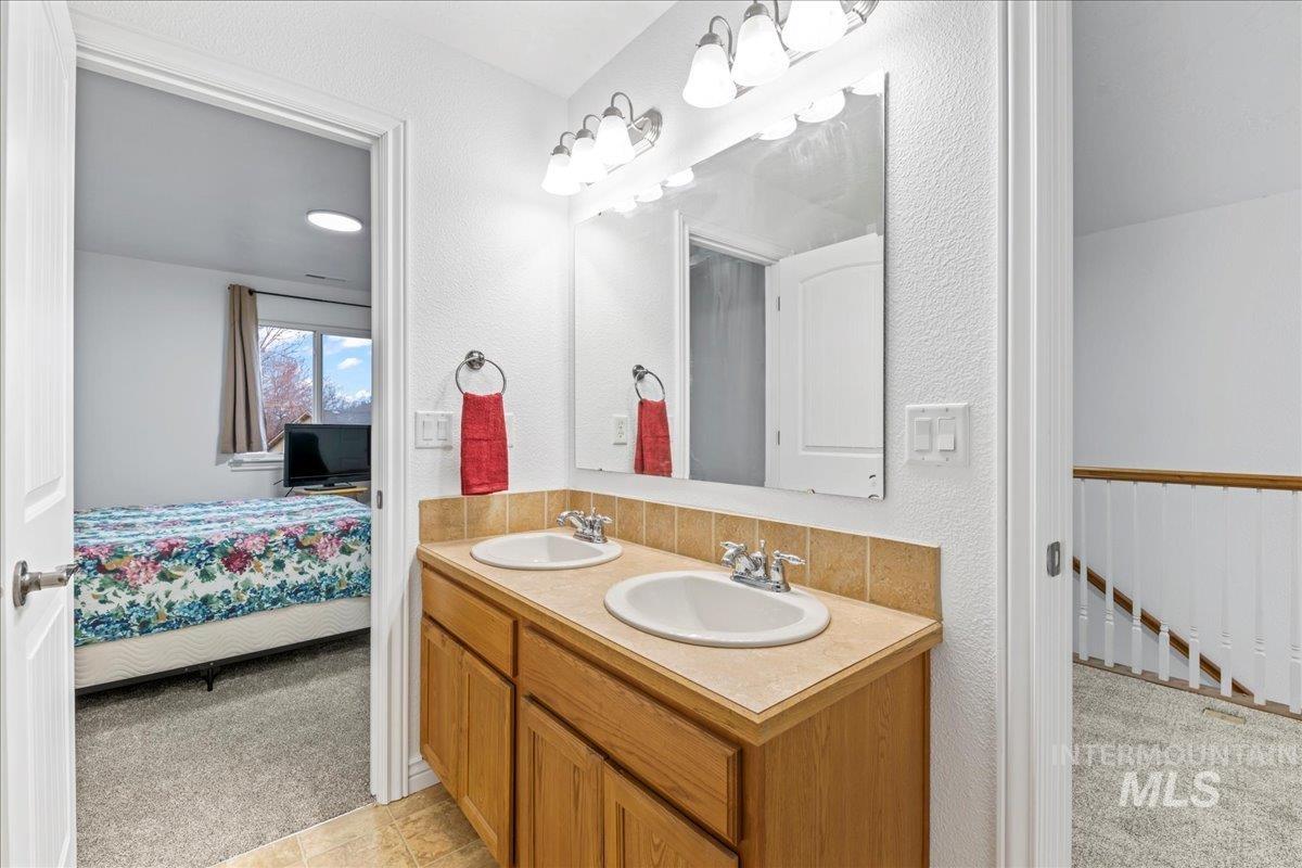 Ensuite bathroom featuring light colored carpet, double vanity, and a textured wall