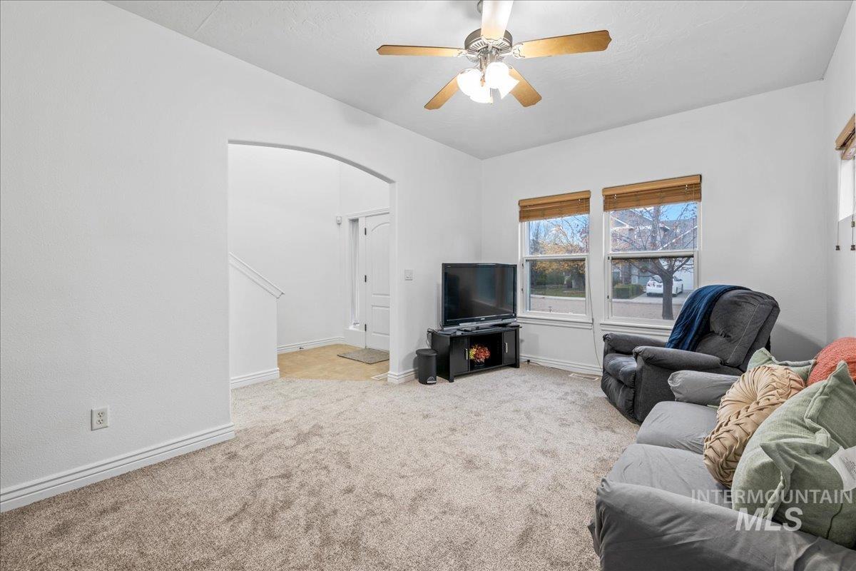 Living room with arched walkways, ceiling fan, and light colored carpet