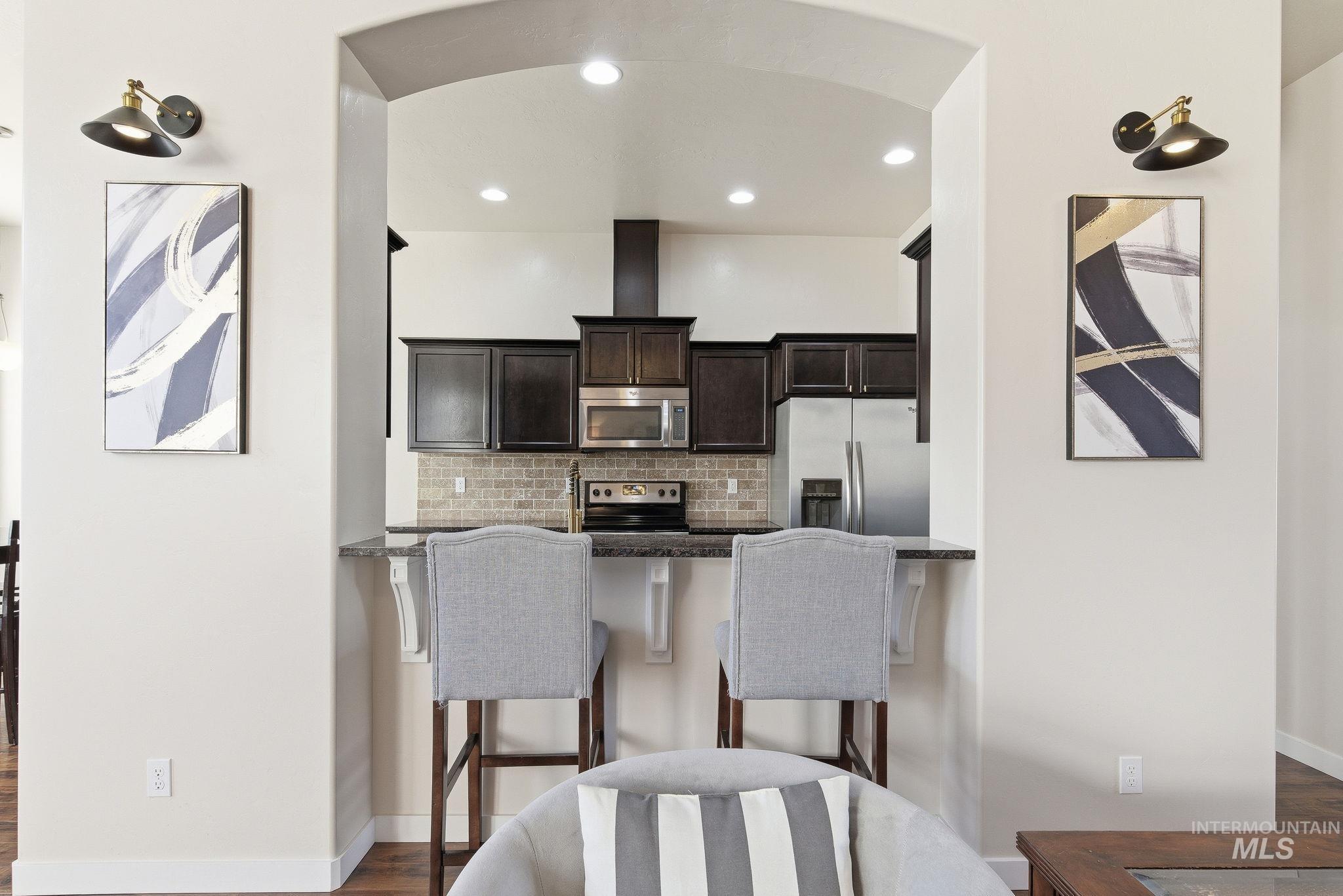 Kitchen featuring appliances with stainless steel finishes, a kitchen breakfast bar, dark brown cabinetry, decorative backsplash, and dark stone counters