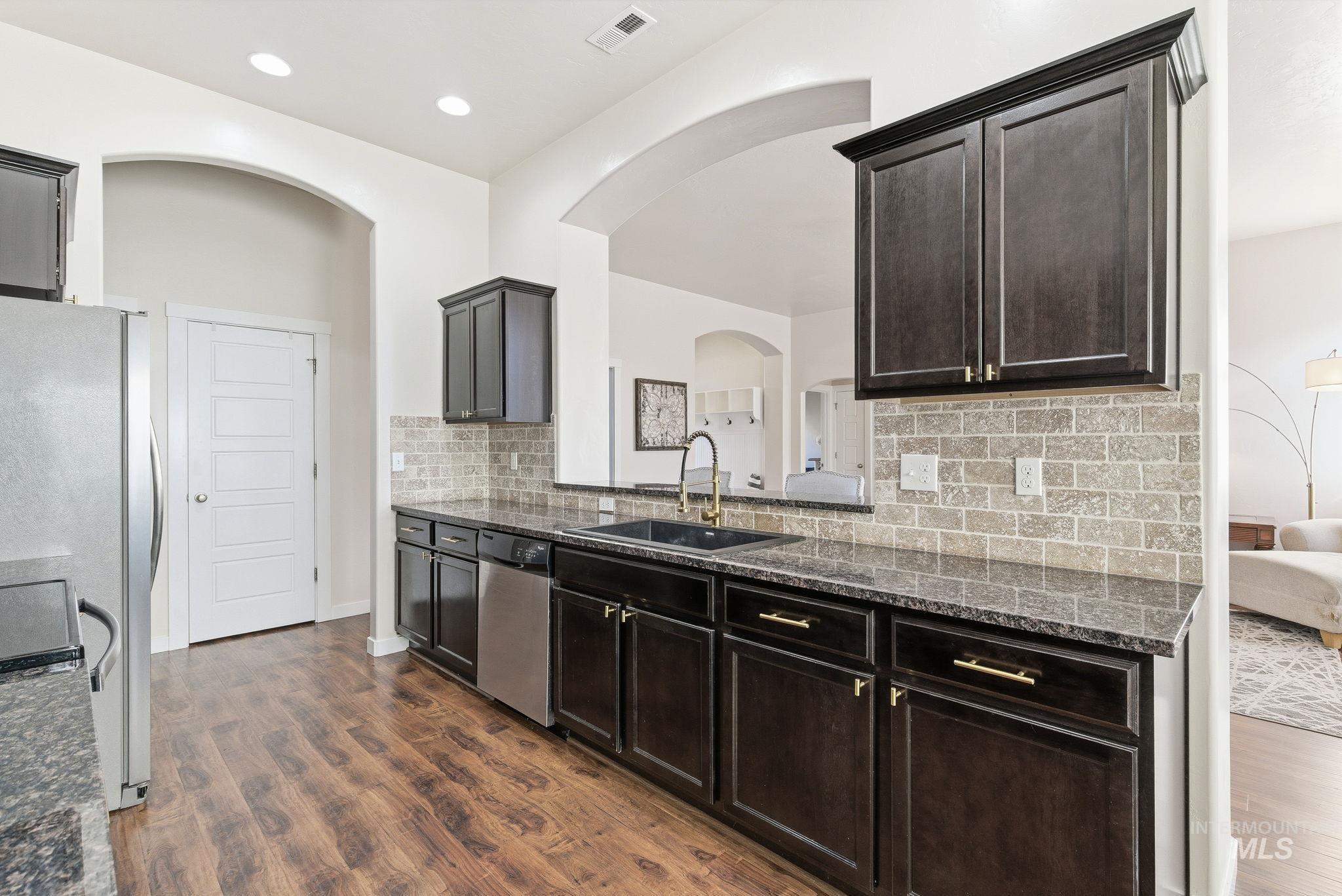 Kitchen featuring dark stone counters, tasteful backsplash, stainless steel appliances, and dark wood-style flooring