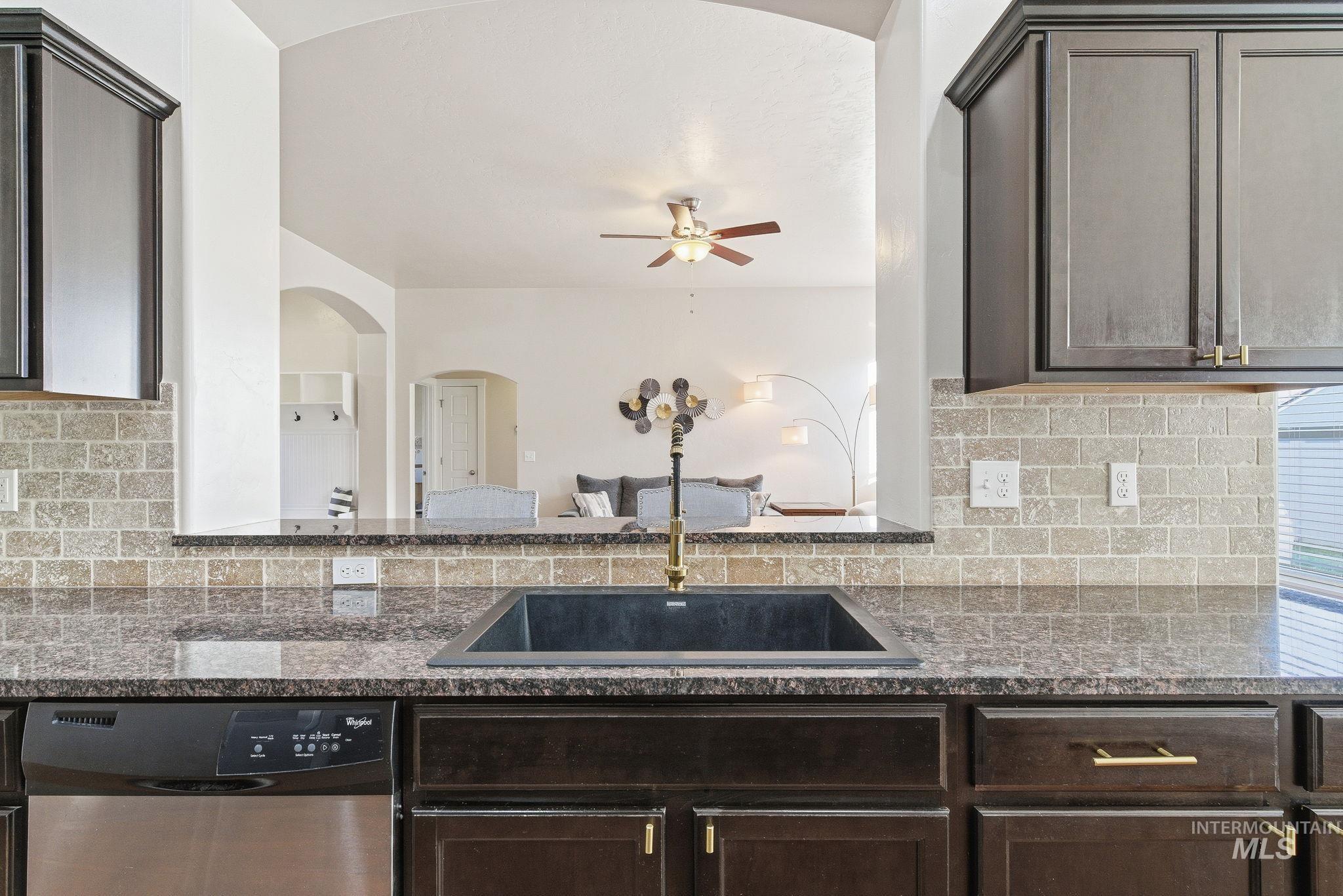Kitchen with dark stone countertops, dishwasher, tasteful backsplash, and dark brown cabinetry