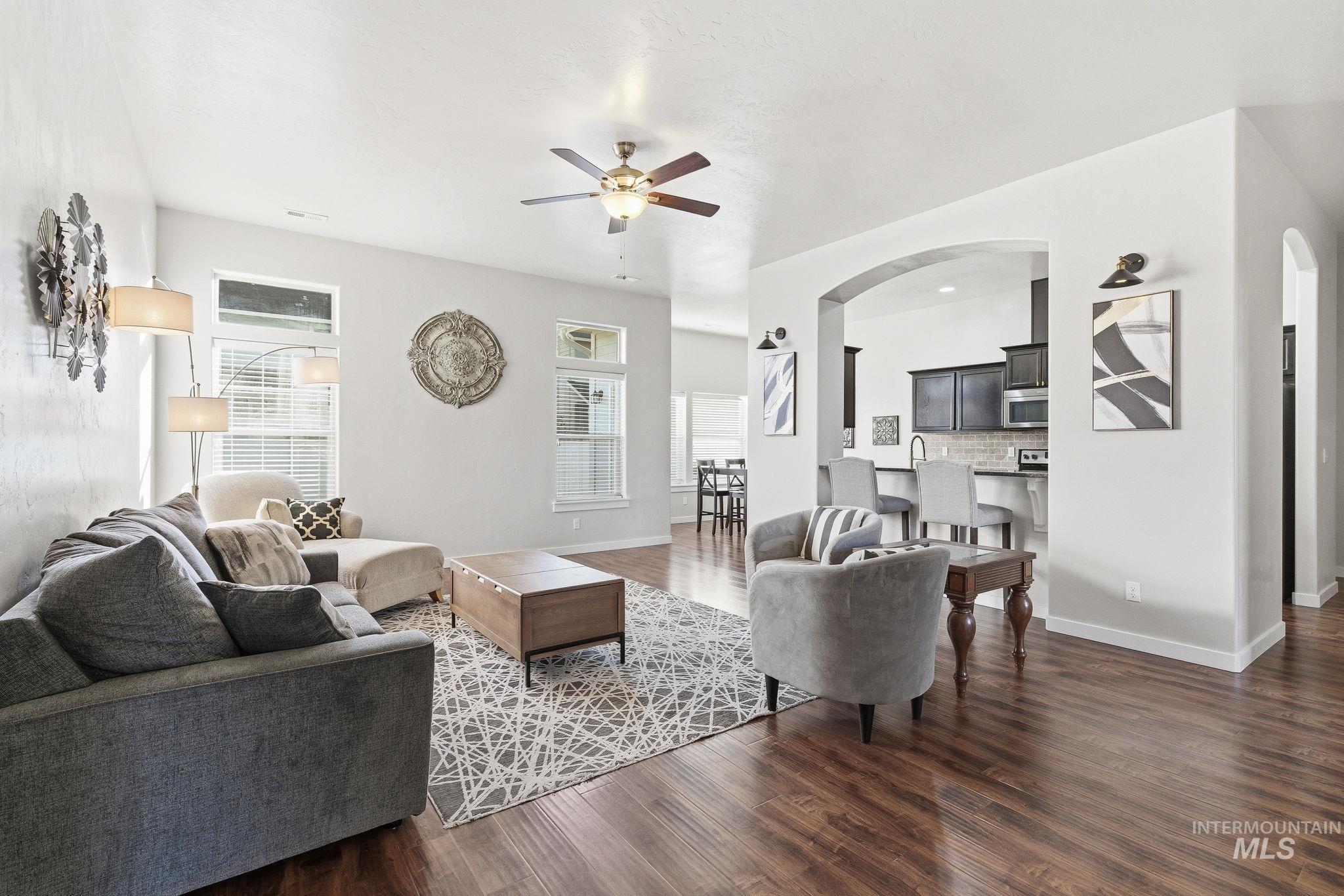 Living area with plenty of natural light, a ceiling fan, dark wood-style flooring, and arched walkways