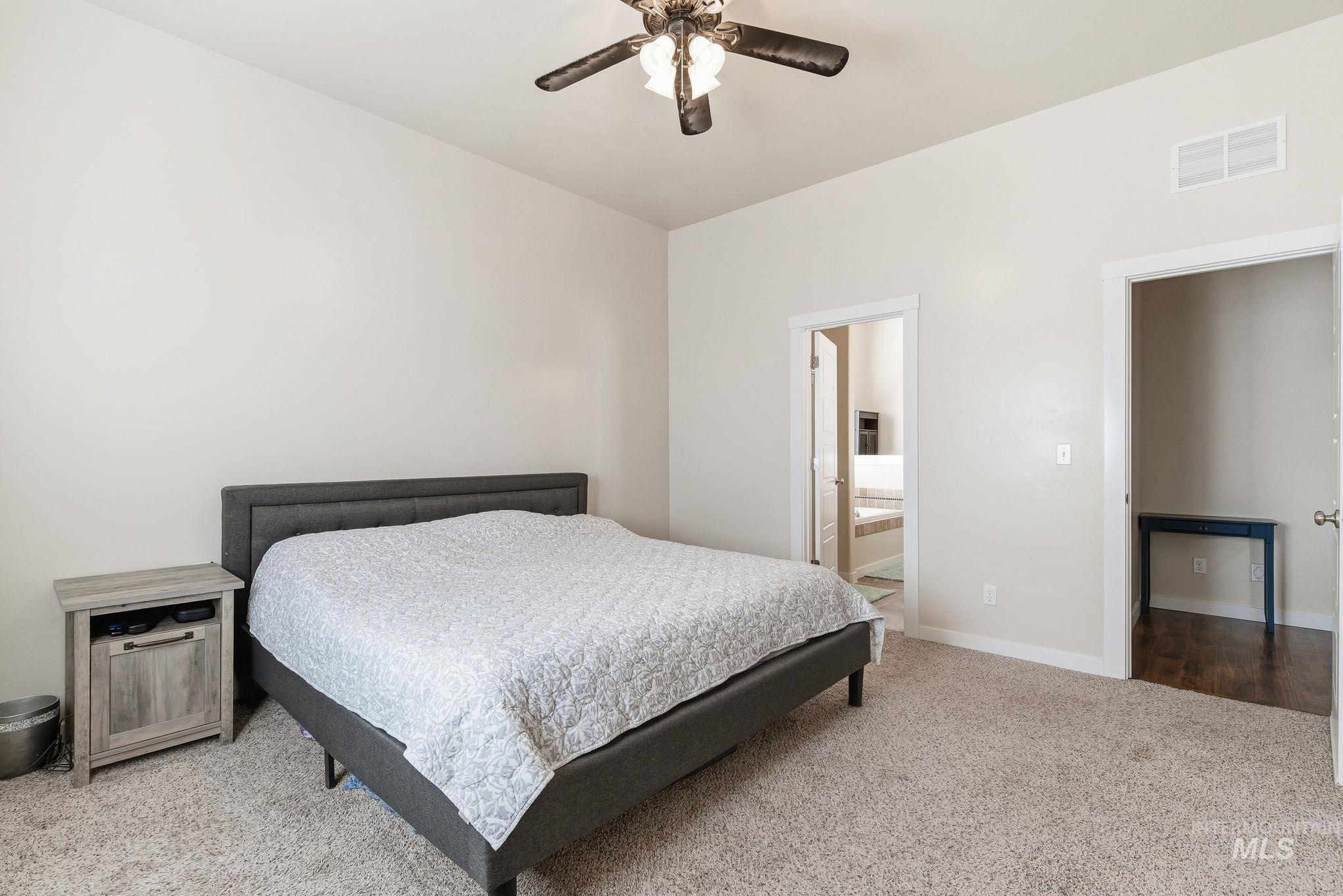 Bedroom featuring light carpet, ensuite bathroom, and a ceiling fan
