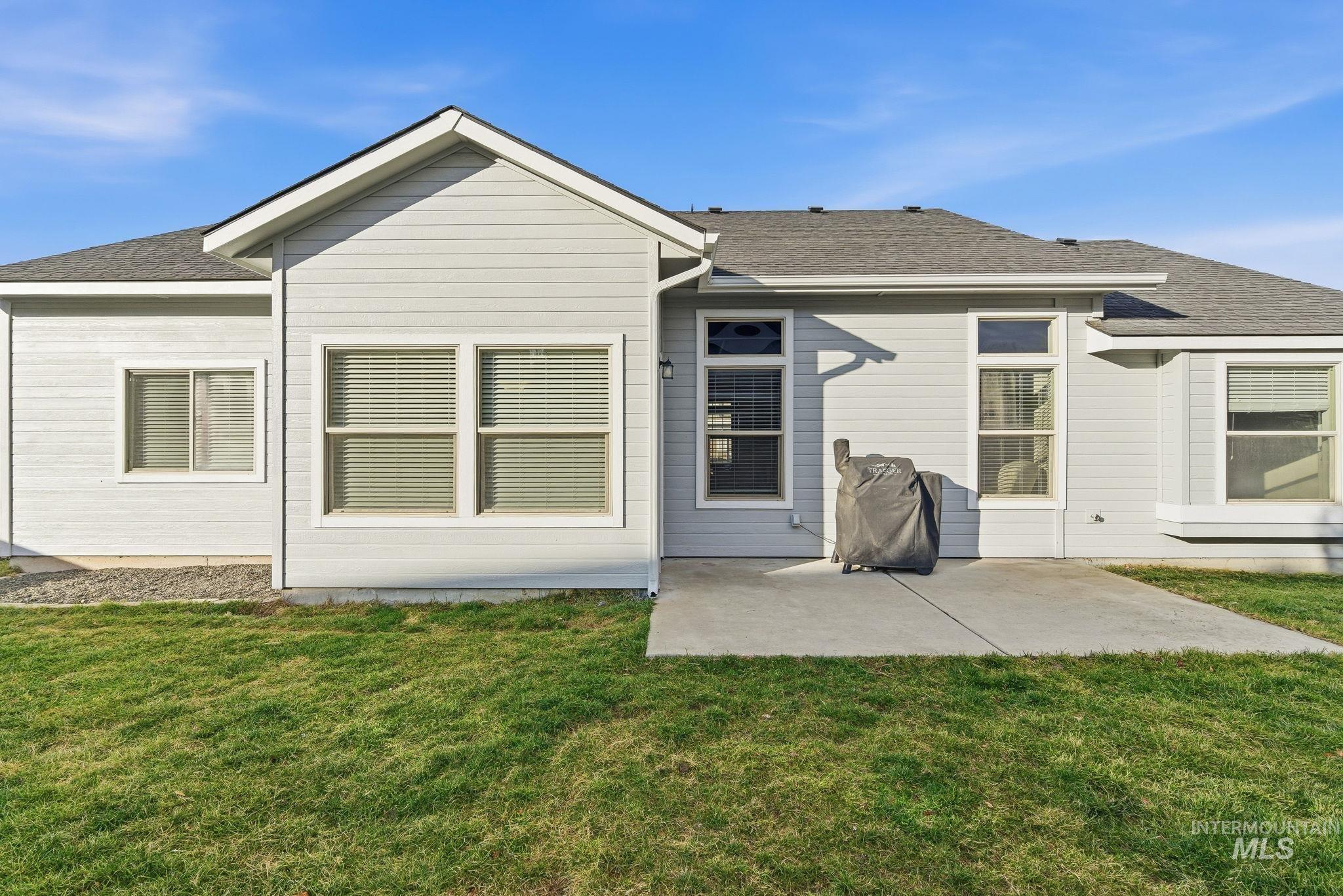Back of property with a shingled roof, a patio, and a yard