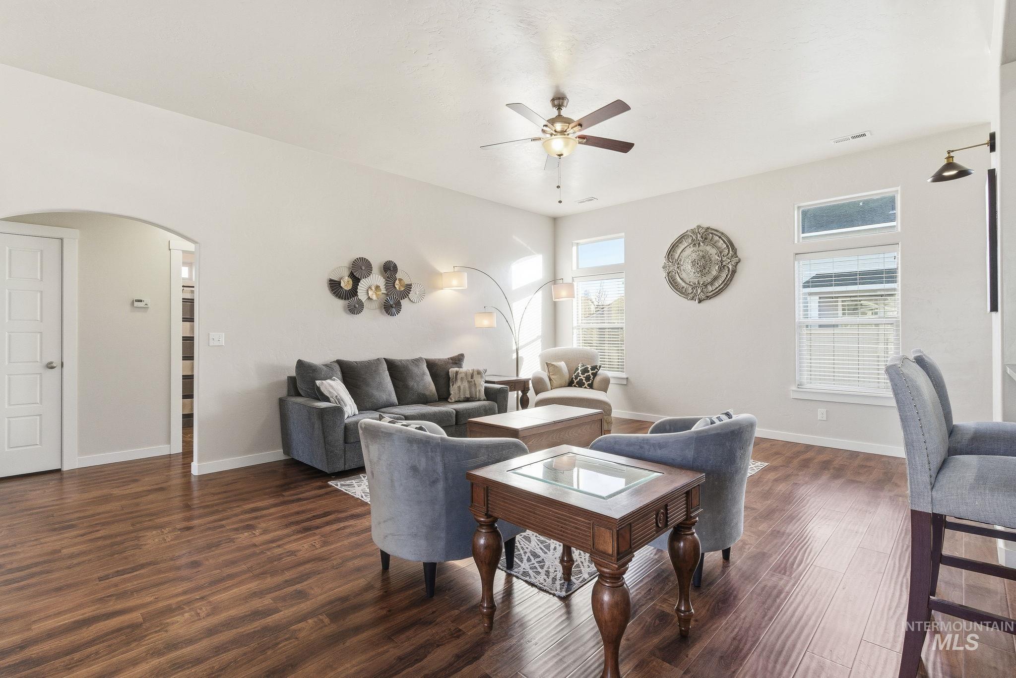 Living room featuring arched walkways, dark wood-style floors, and a ceiling fan