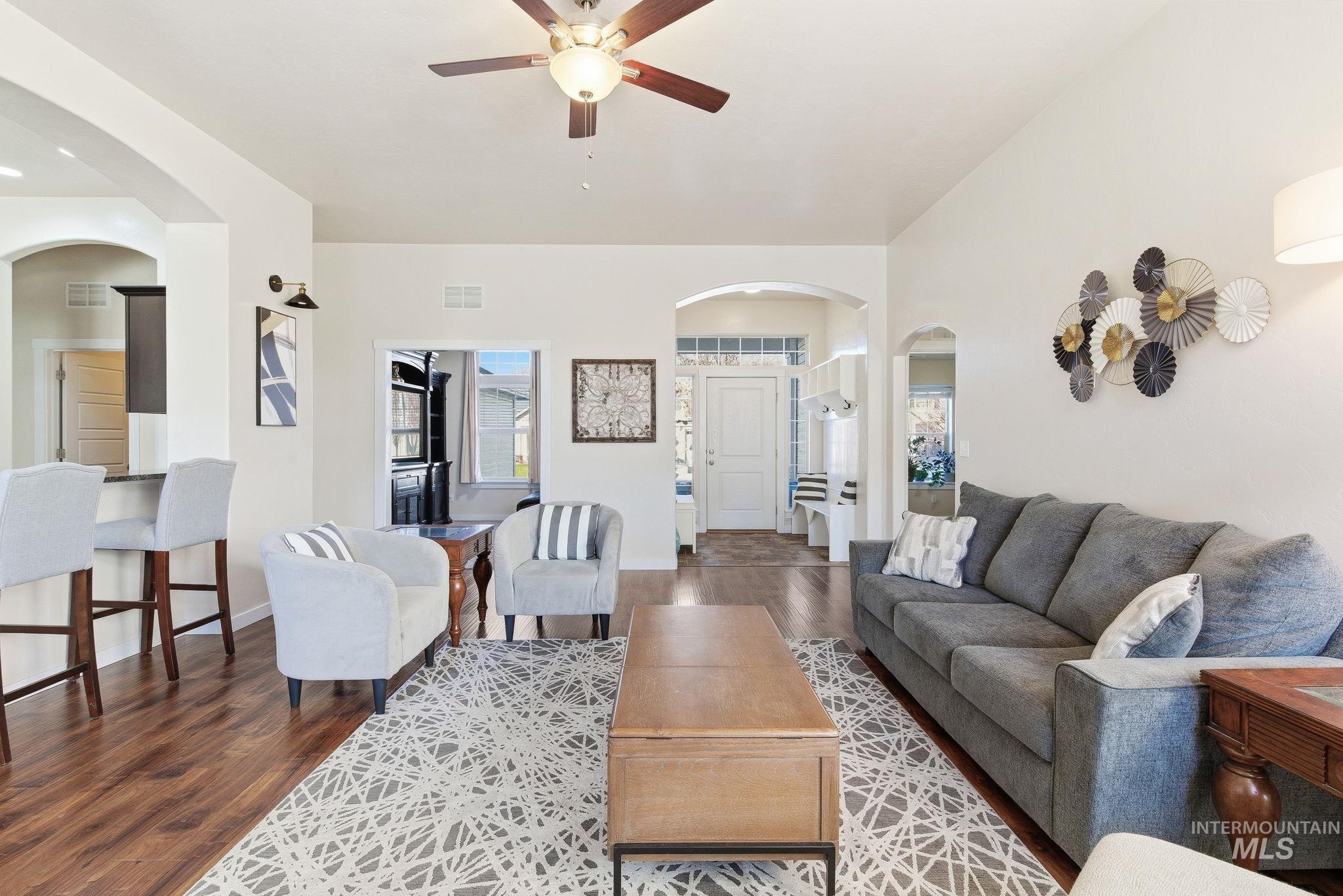 Living room featuring arched walkways, plenty of natural light, dark wood-style floors, and ceiling fan