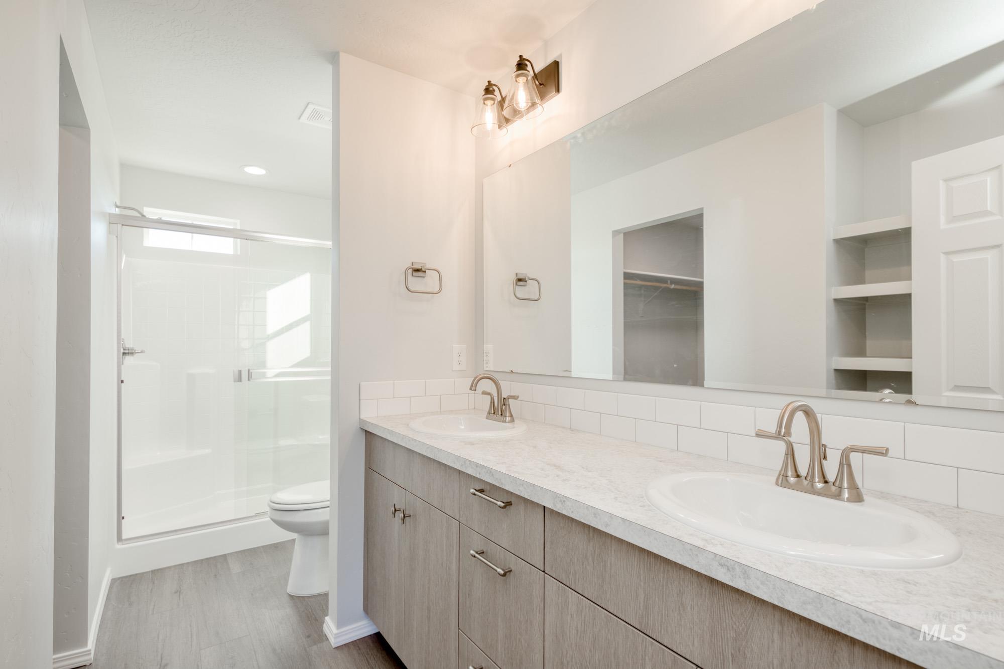 Bathroom featuring a shower stall, double vanity, light wood-style flooring, and backsplash