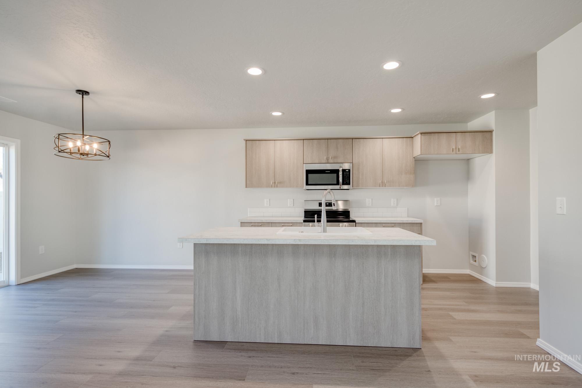 Kitchen featuring light brown cabinetry, recessed lighting, light wood-type flooring, pendant lighting, and stainless steel appliances