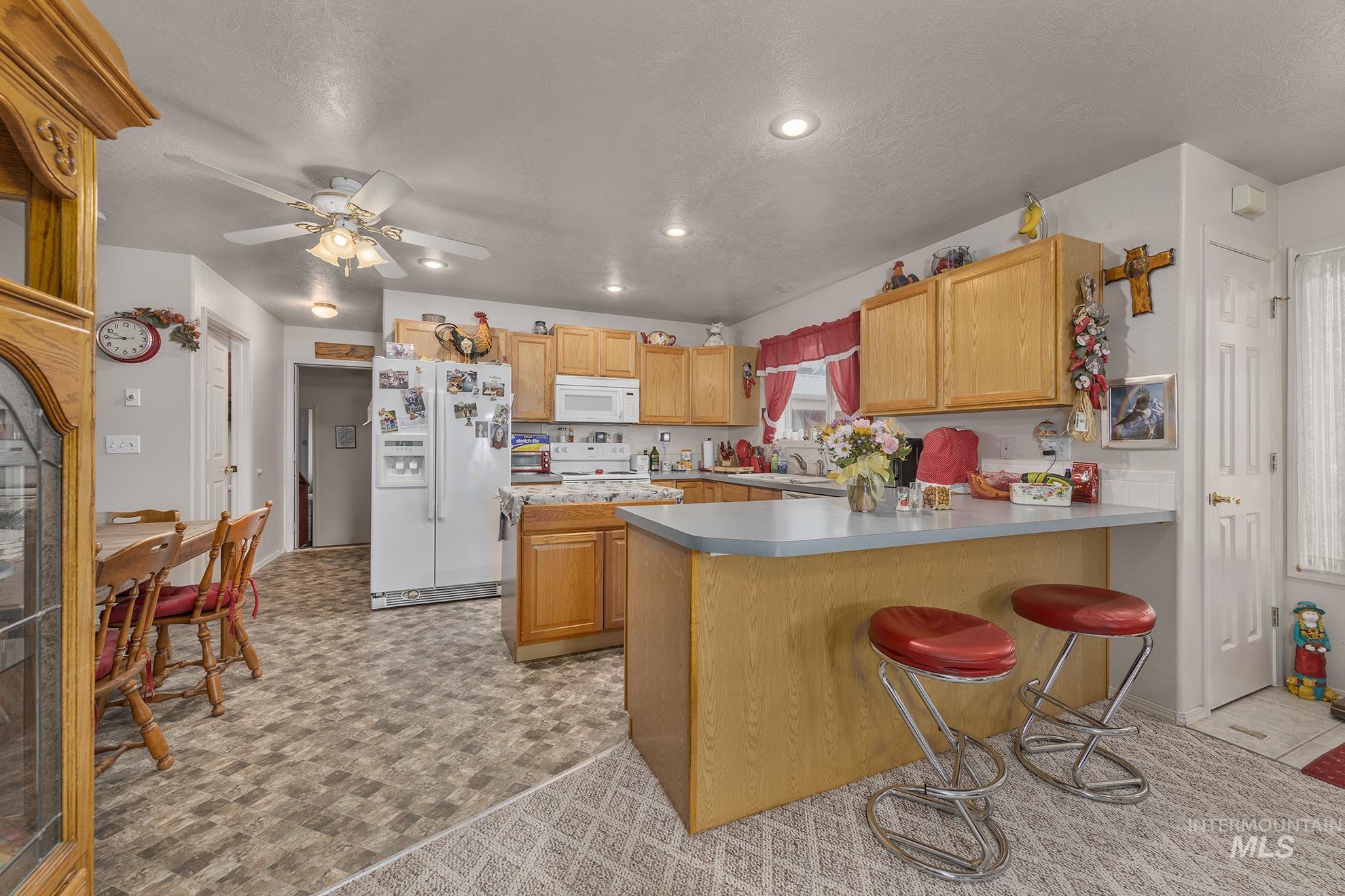 Kitchen featuring white appliances, a kitchen breakfast bar, a peninsula, recessed lighting, and light countertops