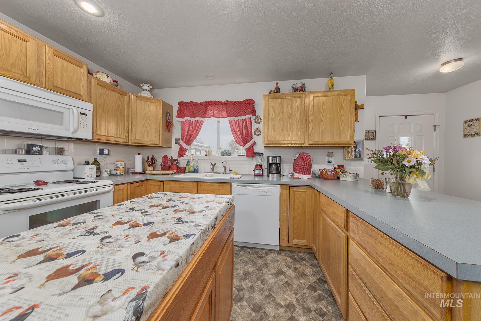 Kitchen featuring white appliances, a peninsula, a textured ceiling, and light countertops