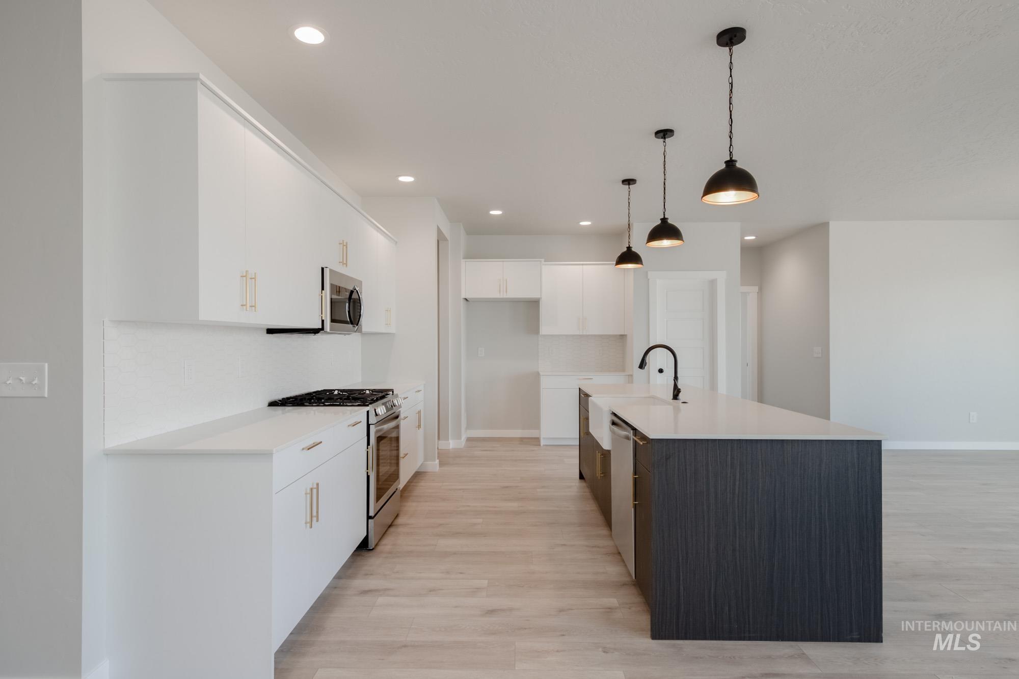 Kitchen with stainless steel appliances, tasteful backsplash, white cabinetry, hanging light fixtures, and light wood finished floors