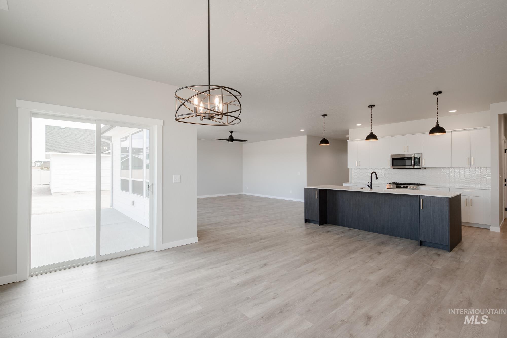 Kitchen featuring white cabinetry, an island with sink, a chandelier, hanging light fixtures, and open floor plan